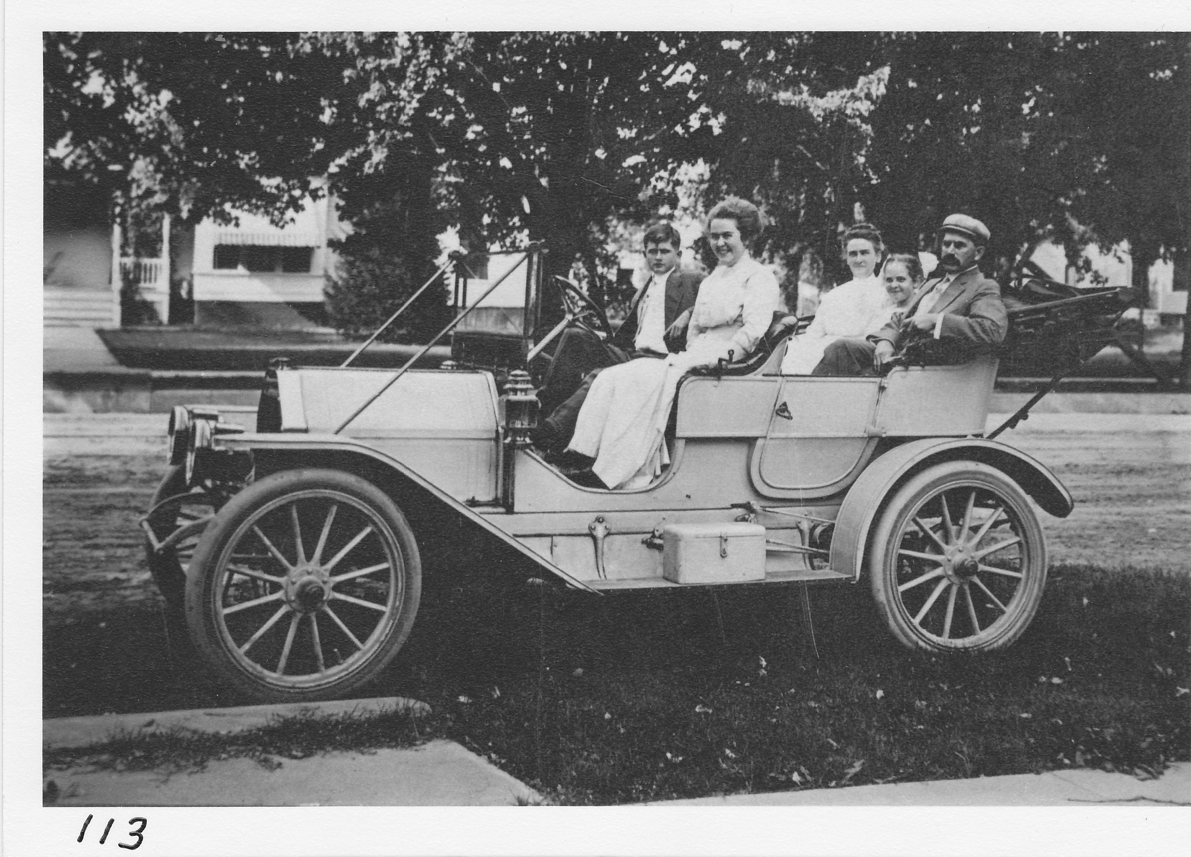 The Buck family in 1908 car at Buck’s corners.  Allie Kennedy home in background, East Main Street and East Street South.  Son Arthur and daughter Alice in front, Mrs. Buck, daughter Winifred, and Mr. Charles Buck in rear.