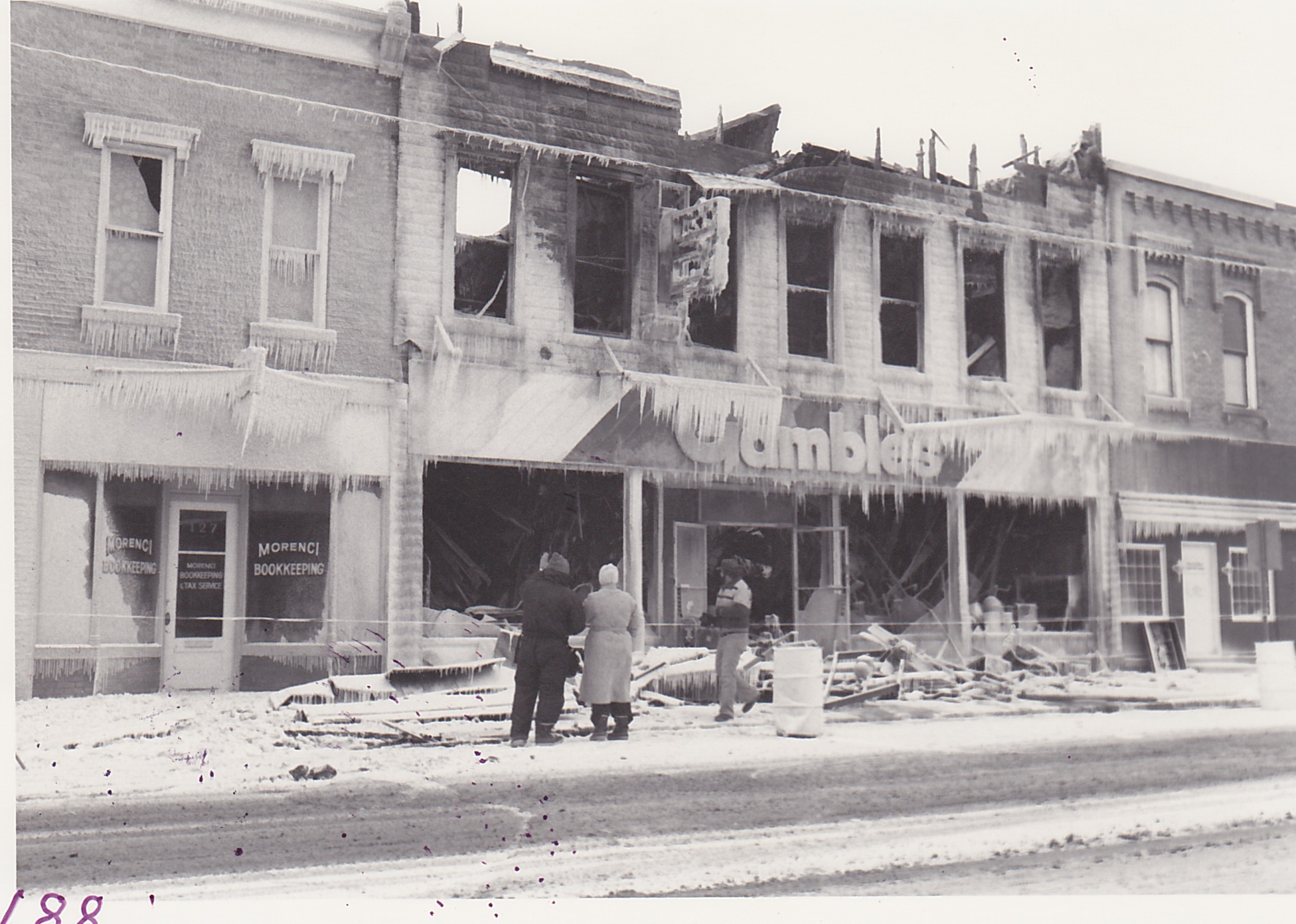 Gamble Store Fire, Jan 19, 1982.  Adam and Gail Johnson (owners) viewing damage the day following the fire.  Temperature was near zero.  Fire started by a burning candle in upstairs apartment.  Building owned by Kenneth Richardson.