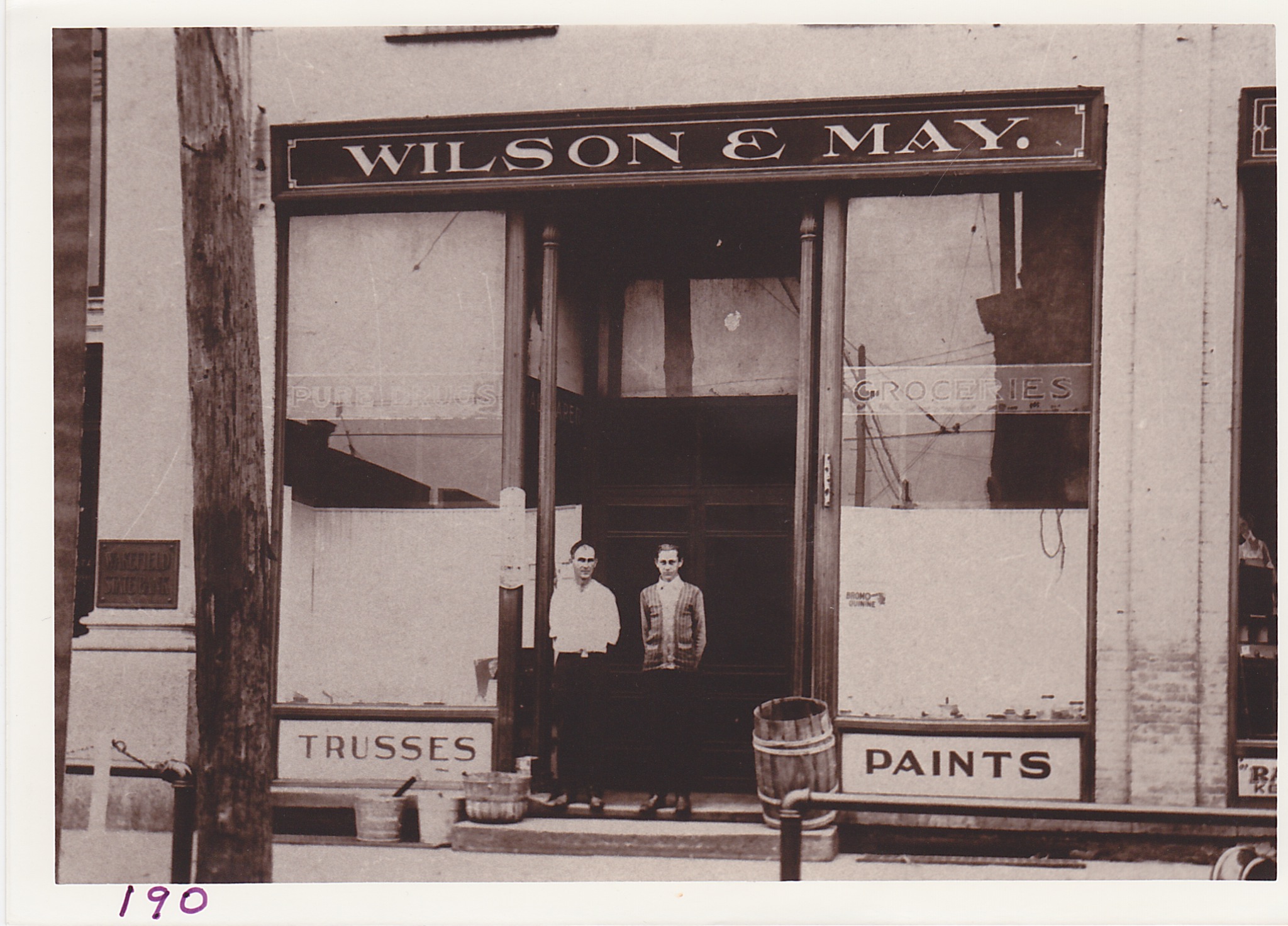 Exterior view of the Wilson-May drug store about 1920. Mr. May is standing on the right while clerk Claude Ranger is on the left. Roscoe Wilson continued as a pharmacist after the partnership was dissolved.