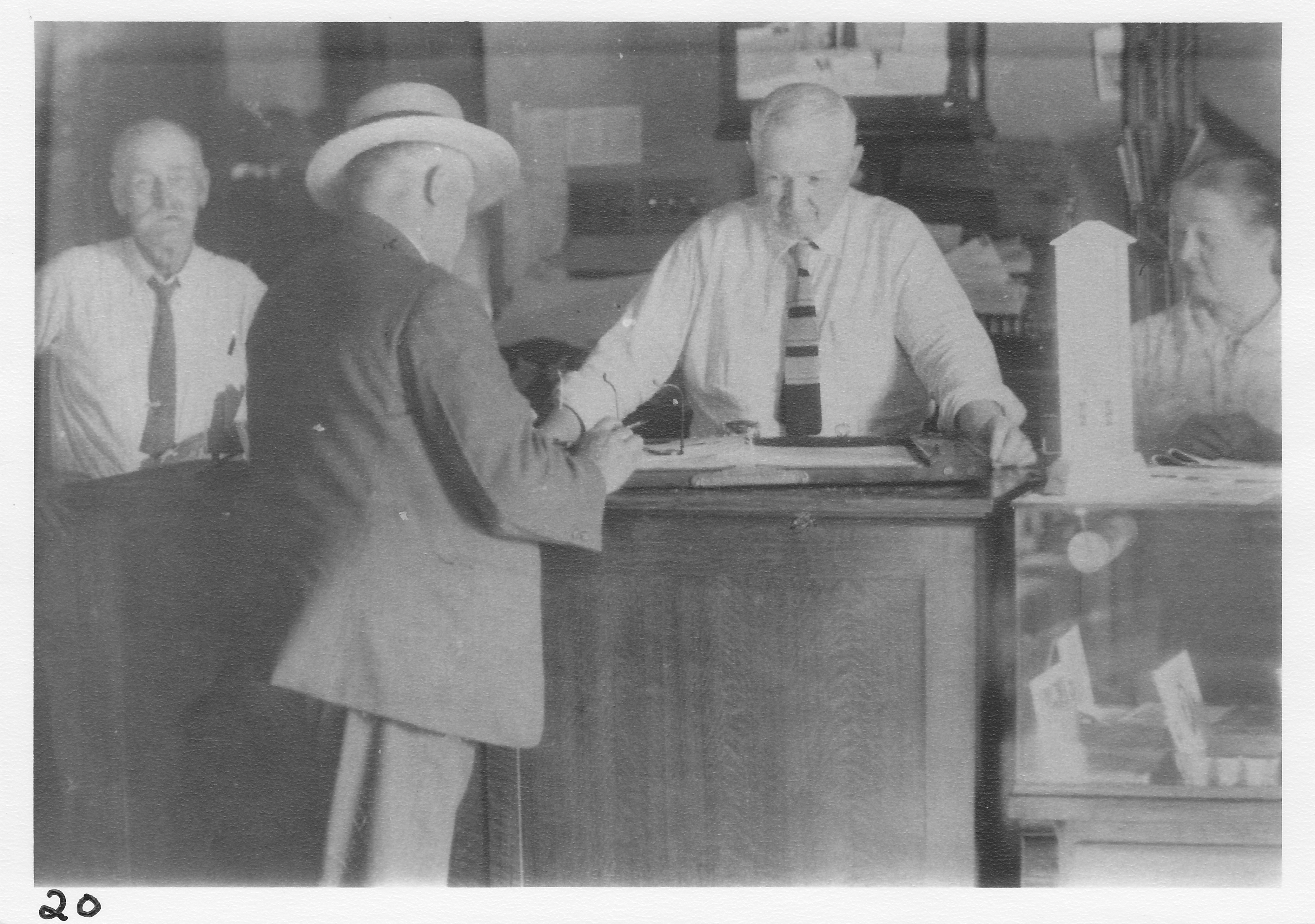 Frank Blair and Mrs. Blair with helper Sam at desk of Hotel Saulsbury registering a guest.