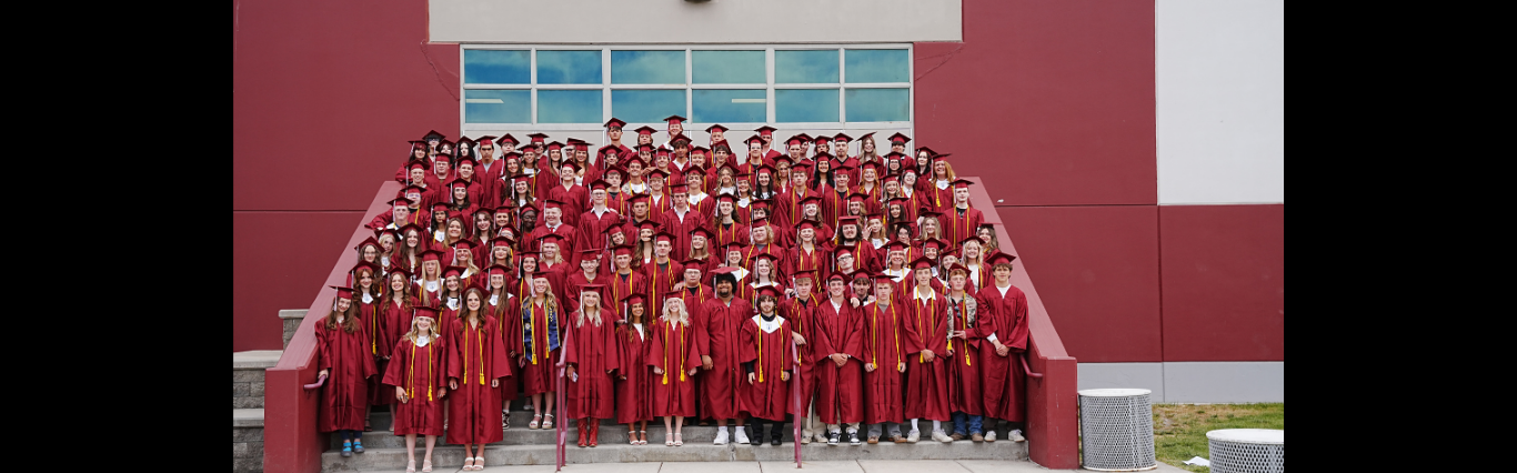 the graduating class of 2026 posing in their red caps &amp; gowns on the steps in front of hamilton high school
