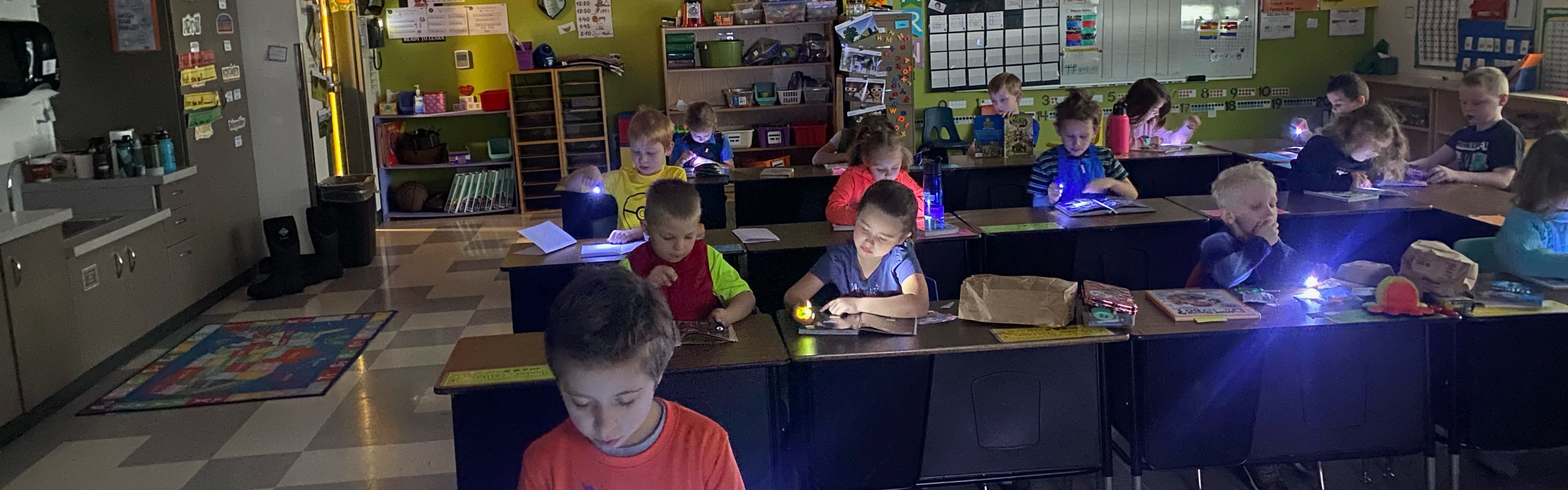 Daly students in a classroom reading books by flashlight