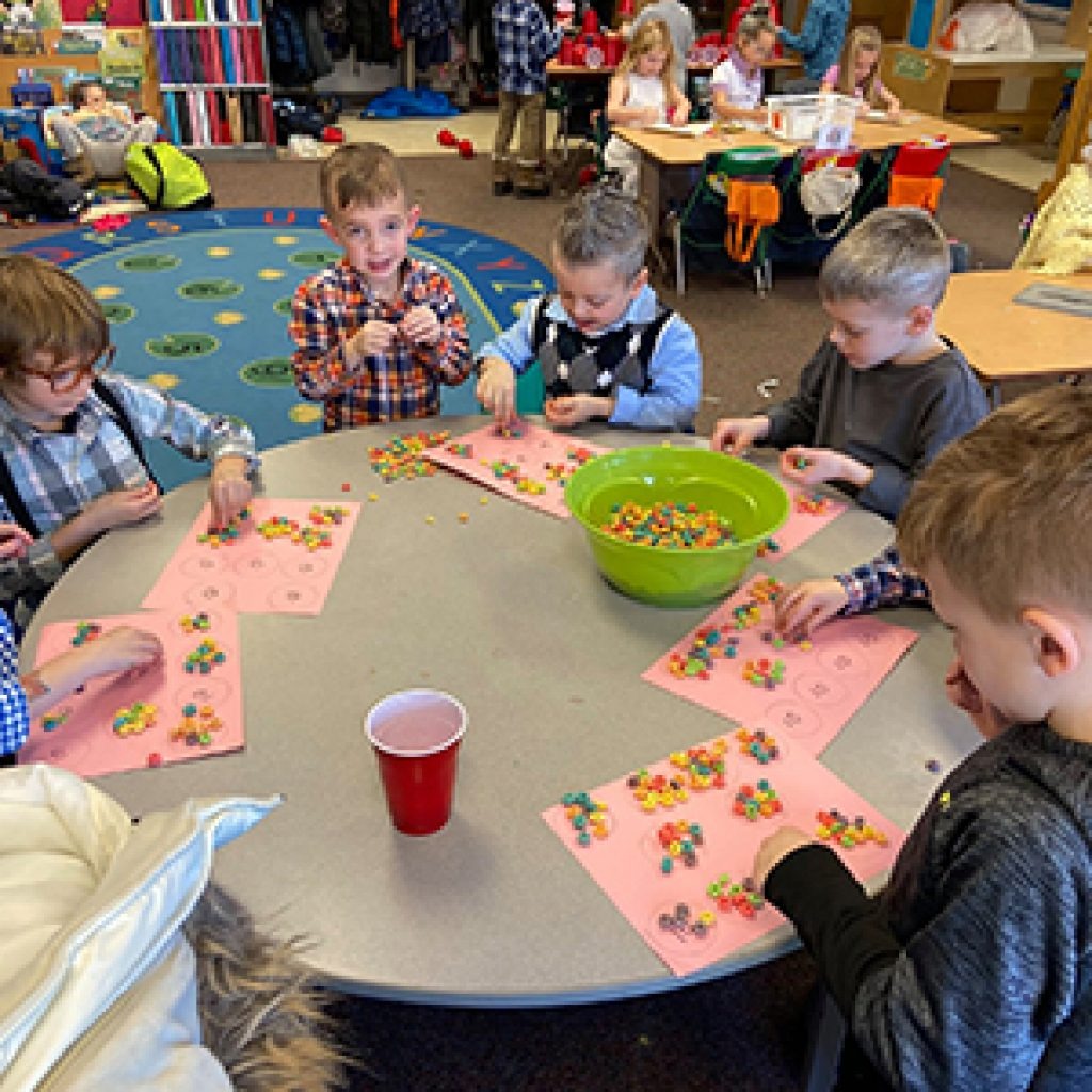 Kindergarten students sitting around a circle table engaged in a counting activity using beads.