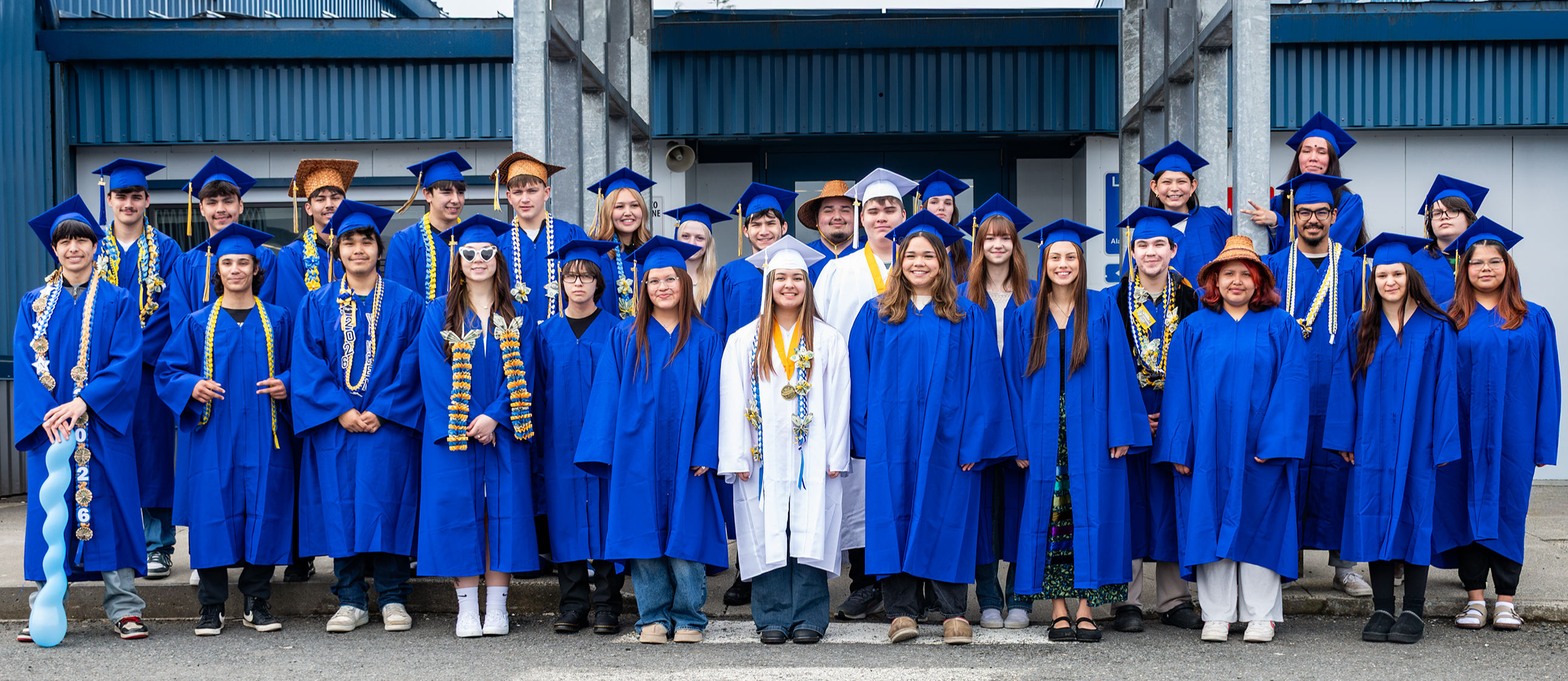 students in front of school in graduation caps and gowns.  