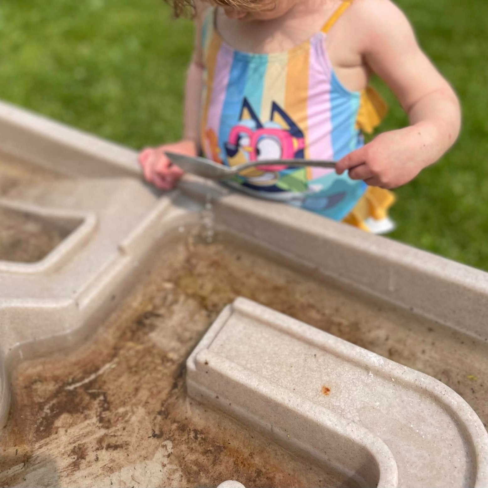 child using spoon in sensory table outdoors