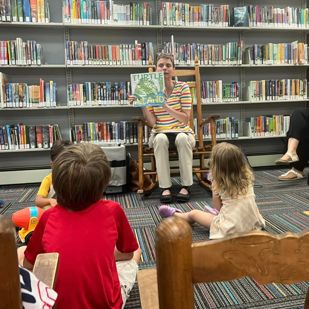 children listening to a book being read by librarian at local library