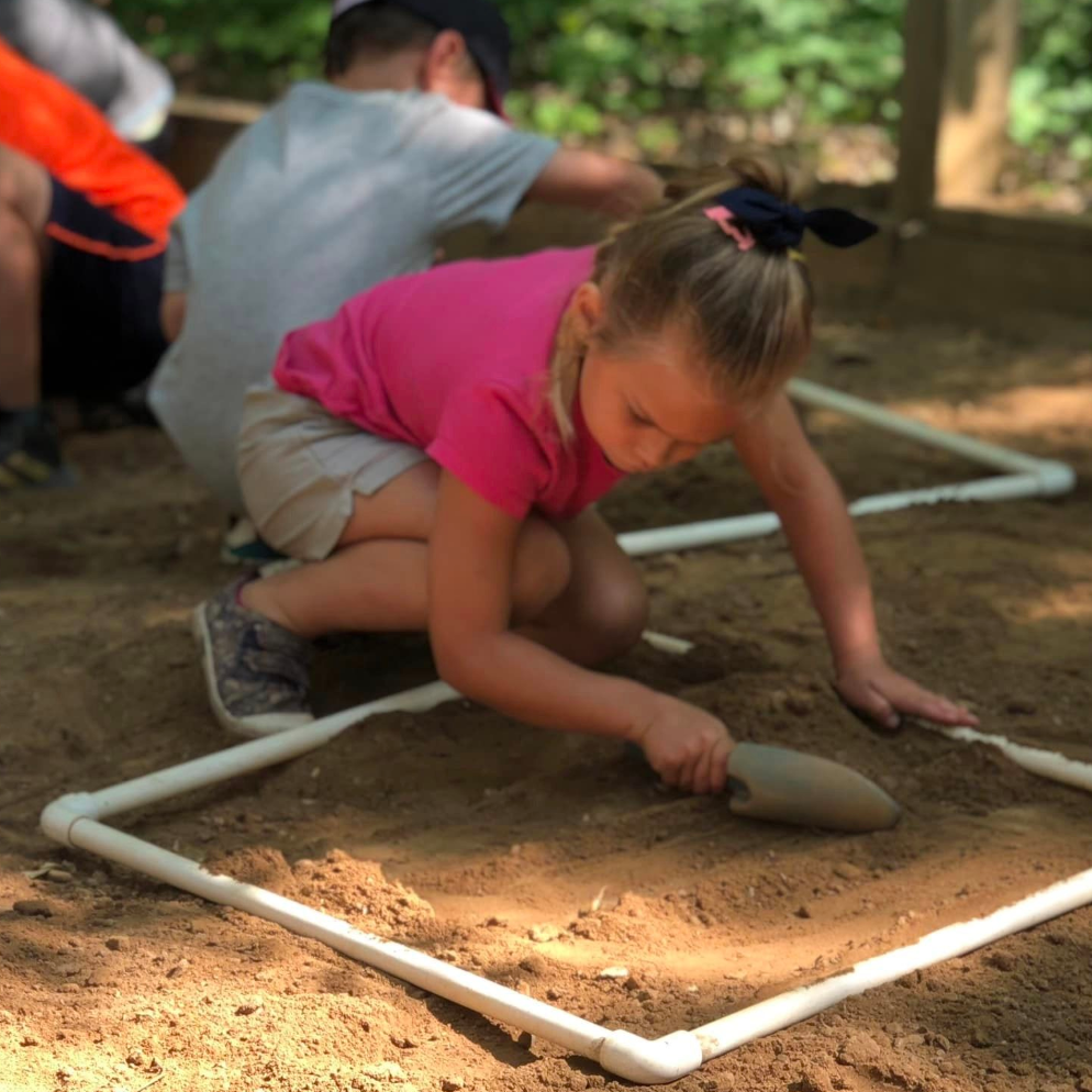 child digging in dirt with shovel, outdoors