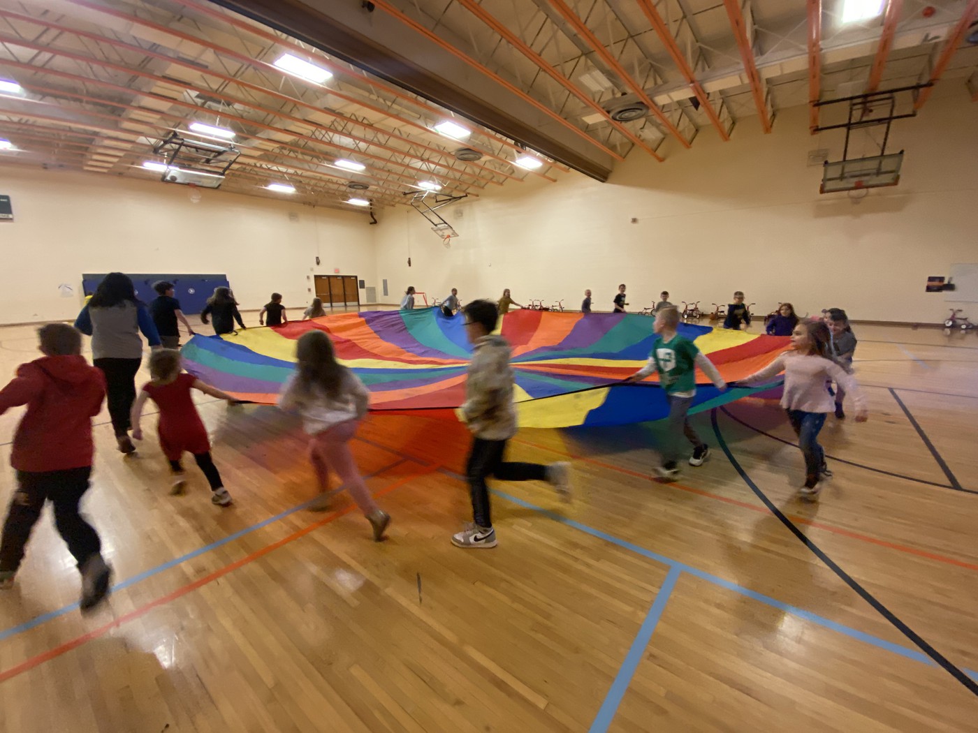 children running around large colorful parachute in gym