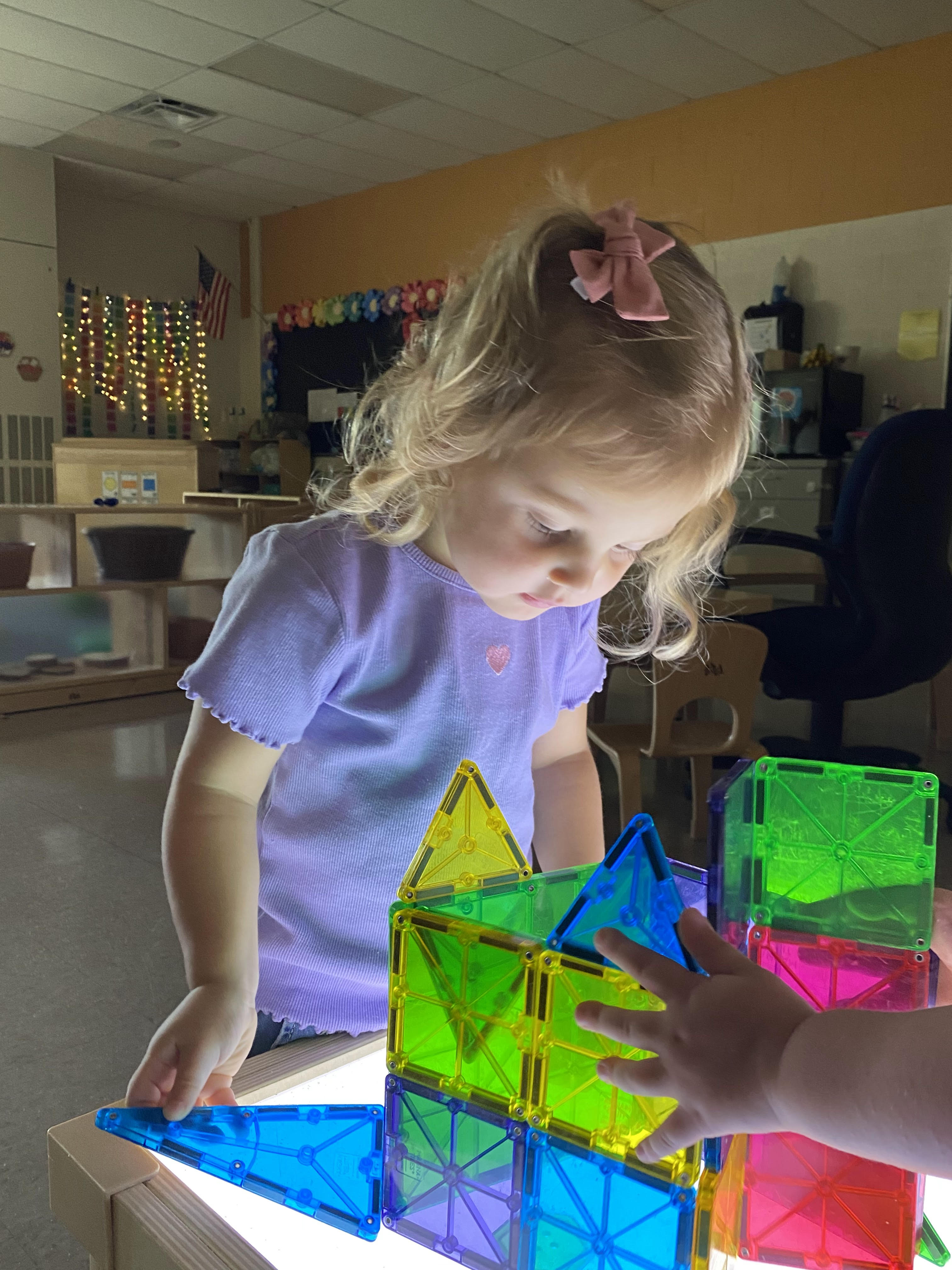 toddler girl building with magnets on light table in classroom