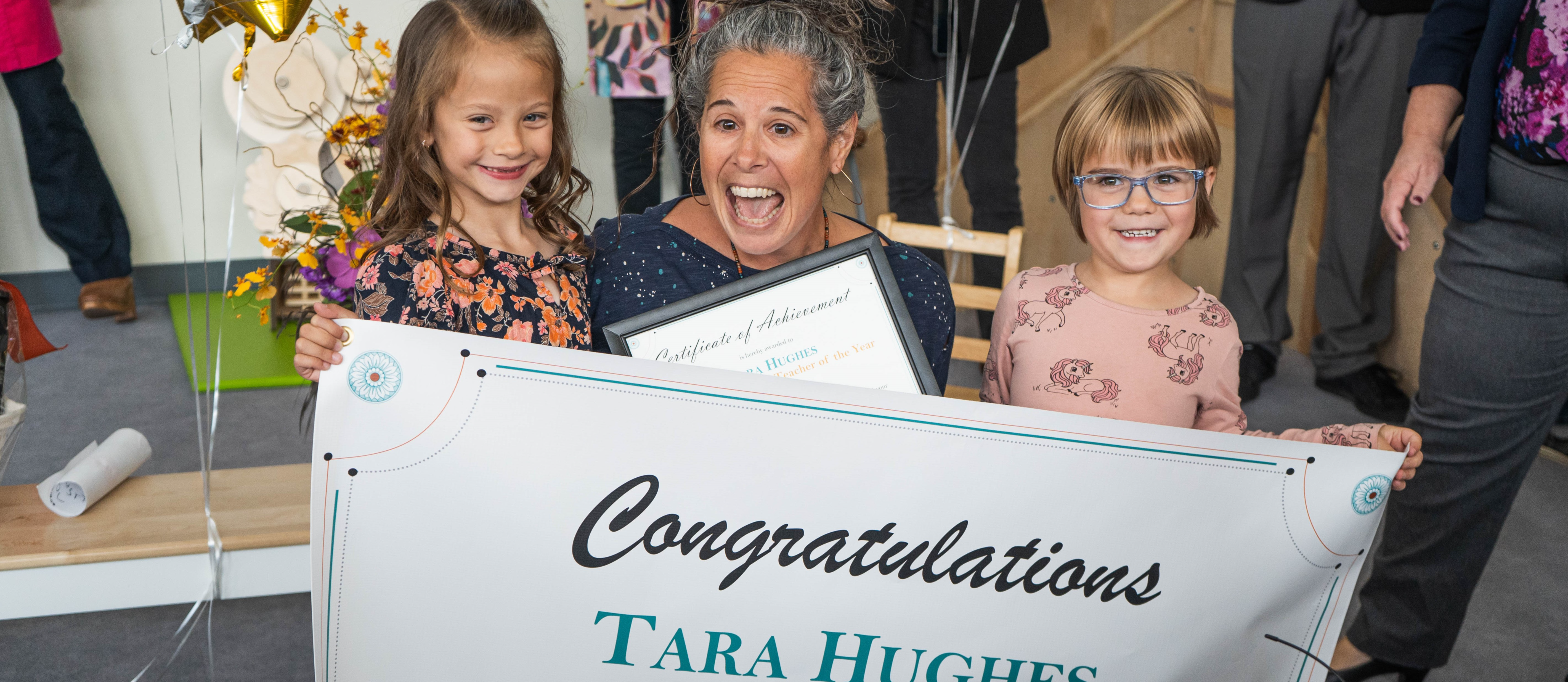 Tara Hughes holding a banner "Congratulations Tara Hughes" with two of her female students