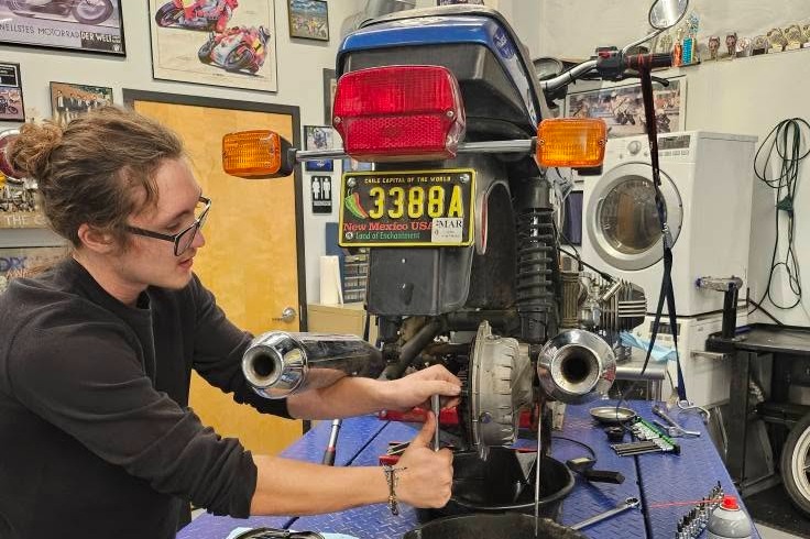 A woman is using a wrench to work on a motorcycle's engine on a blue table.