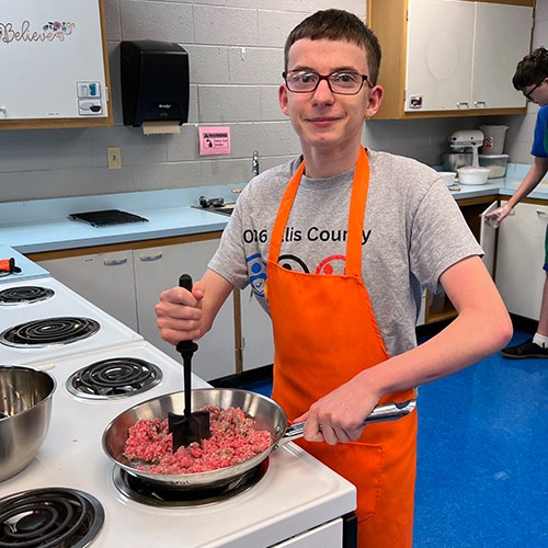 teenage boy frying hamburger in home economics class