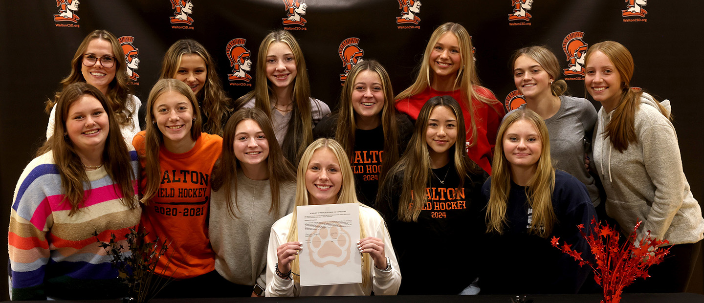 Student signs letter of intent and surrounded by her teammates