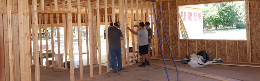 students and instructor working on frame of house that has yet to be dry walled