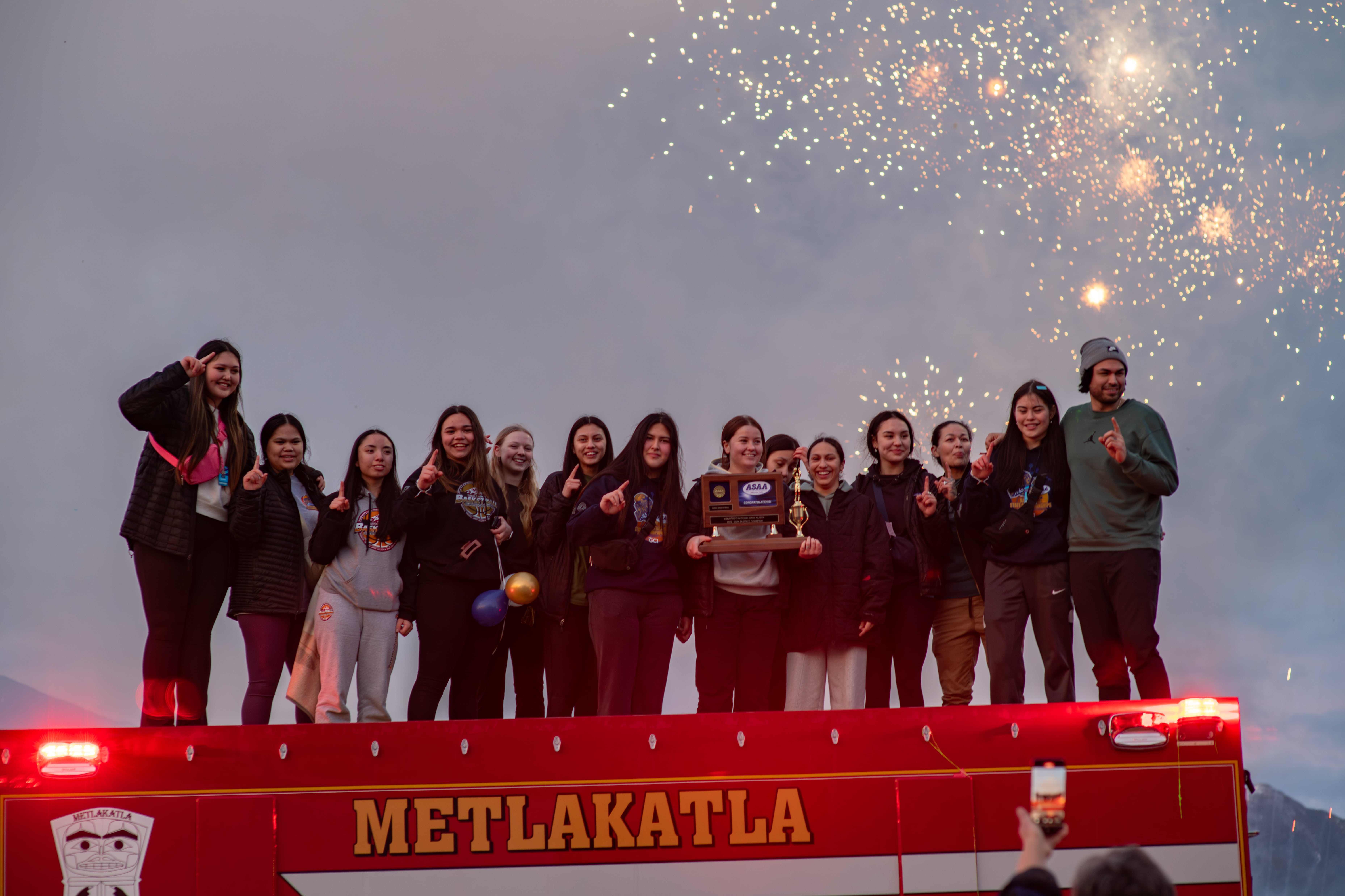 students standing on top of fire truck with fireworks in background