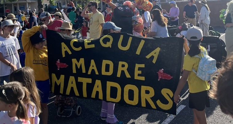 Indoor basketball court with a black curtain backdrop. A yellow banner reading "GO MATADORS" lies on the floor.