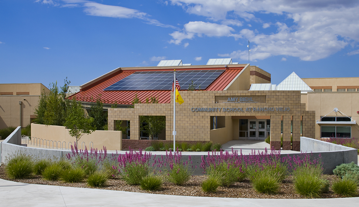 A building with solar panels on the roof and a flag. A yellow flag flies on a pole.
