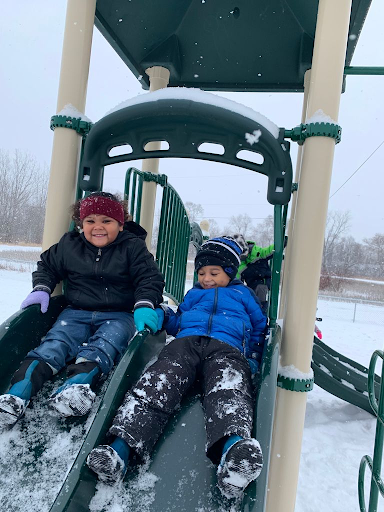 Two young boys slide down slide outside wearing winter gear