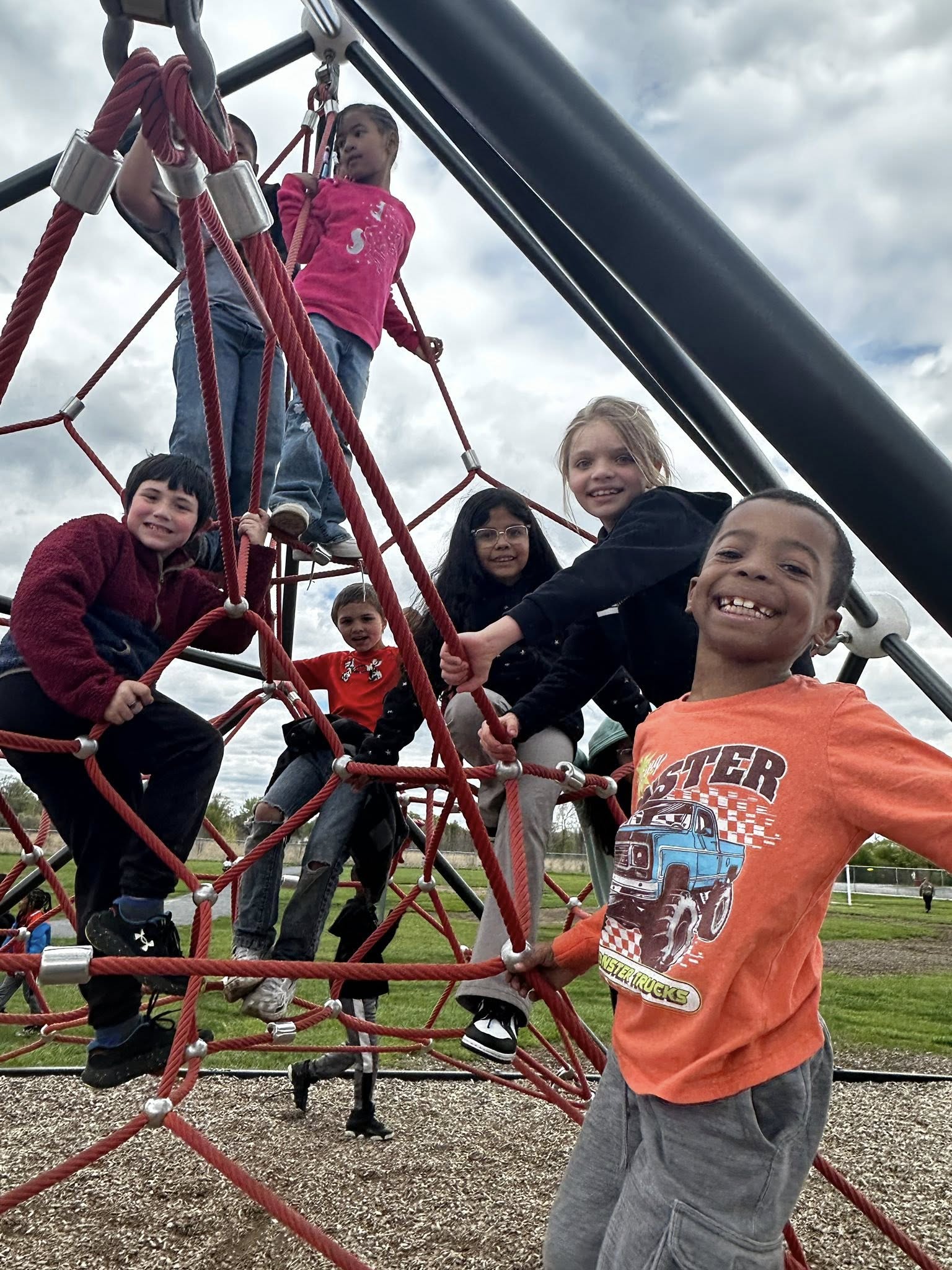 a group of elementary students smiling as they sit at various levels on a piece of climbing playground equipment