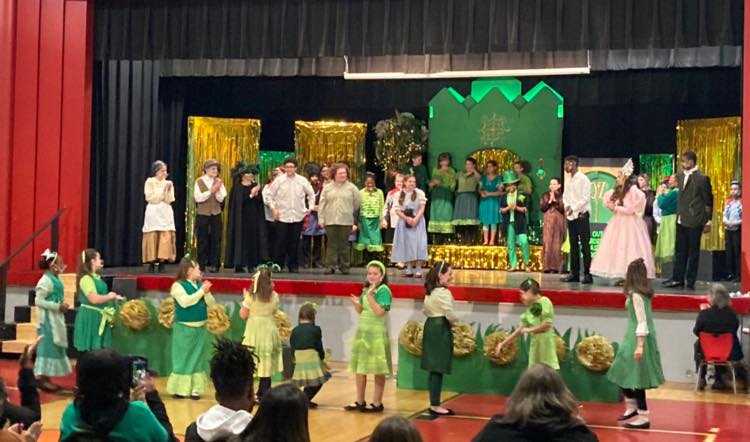 Students stand on stage and on main floor performing Wizard of Oz in costume