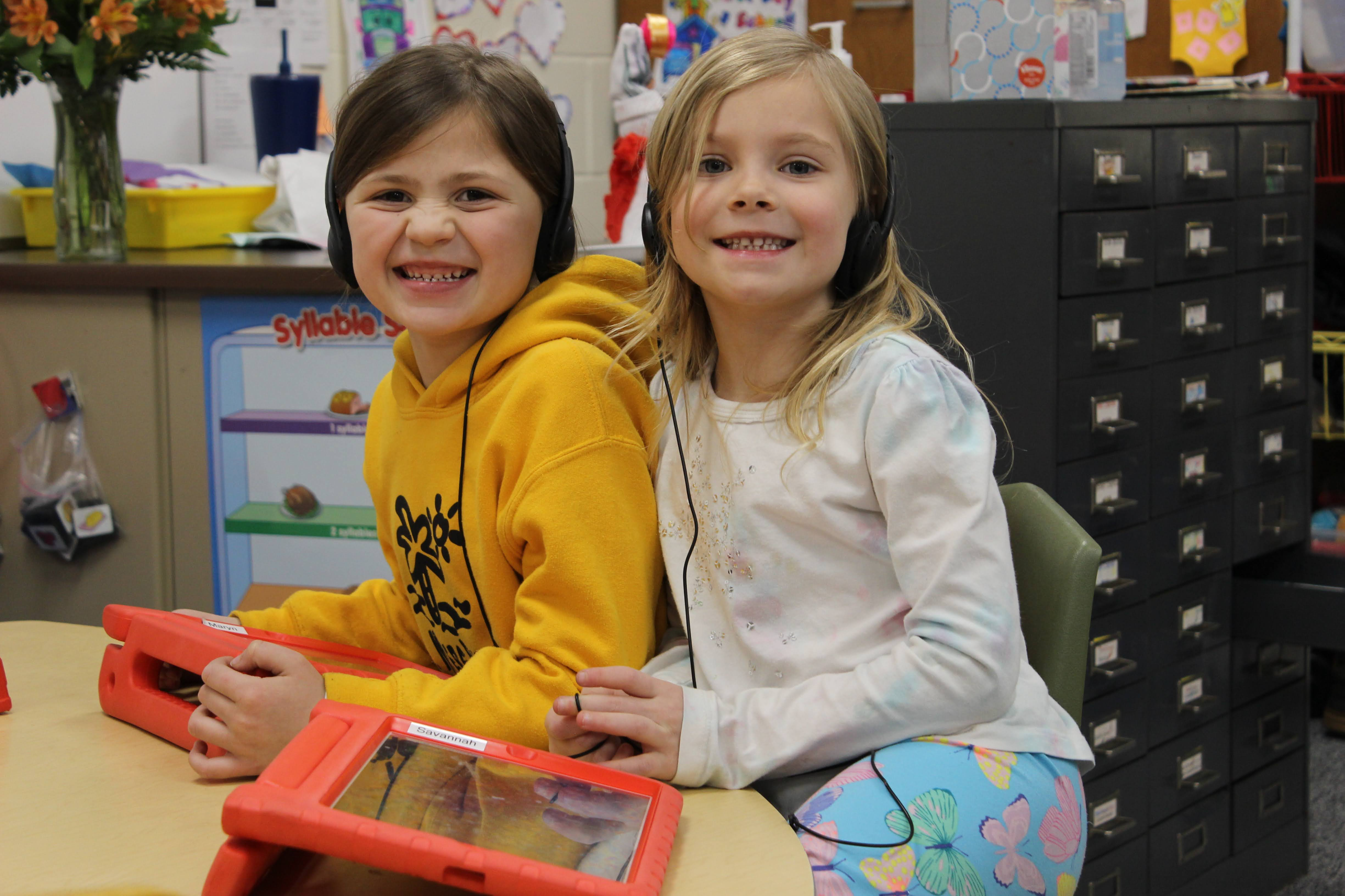 Two girls with headphones on using technology