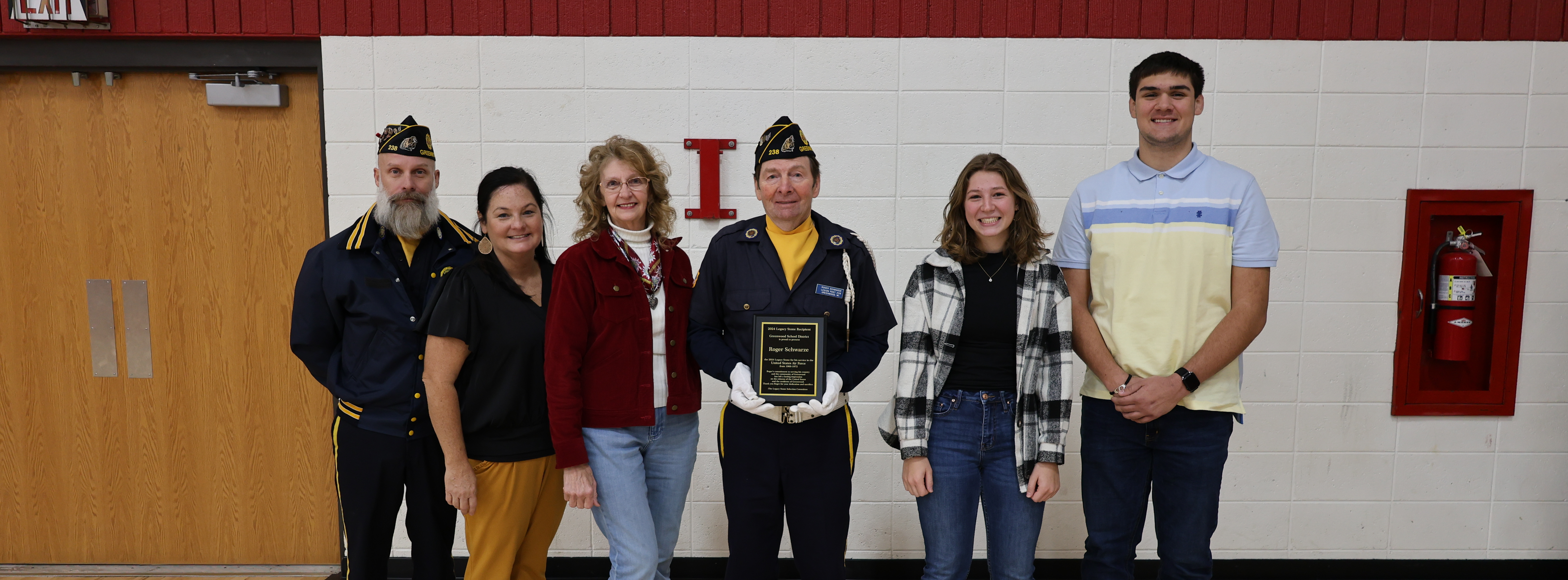 six men and women standing with a veteran holding a plaque