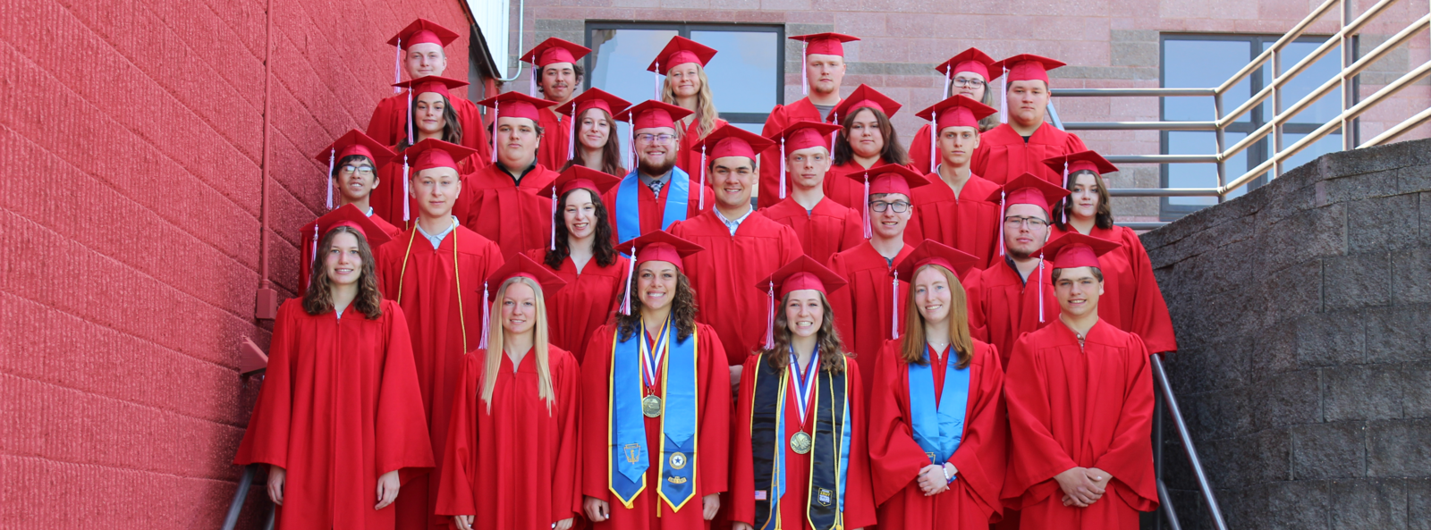 class of 2025 standing on steps in red cap and gown