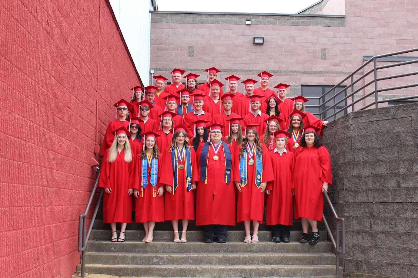 students wearing red graduation robes and caps, standing in rows on steps