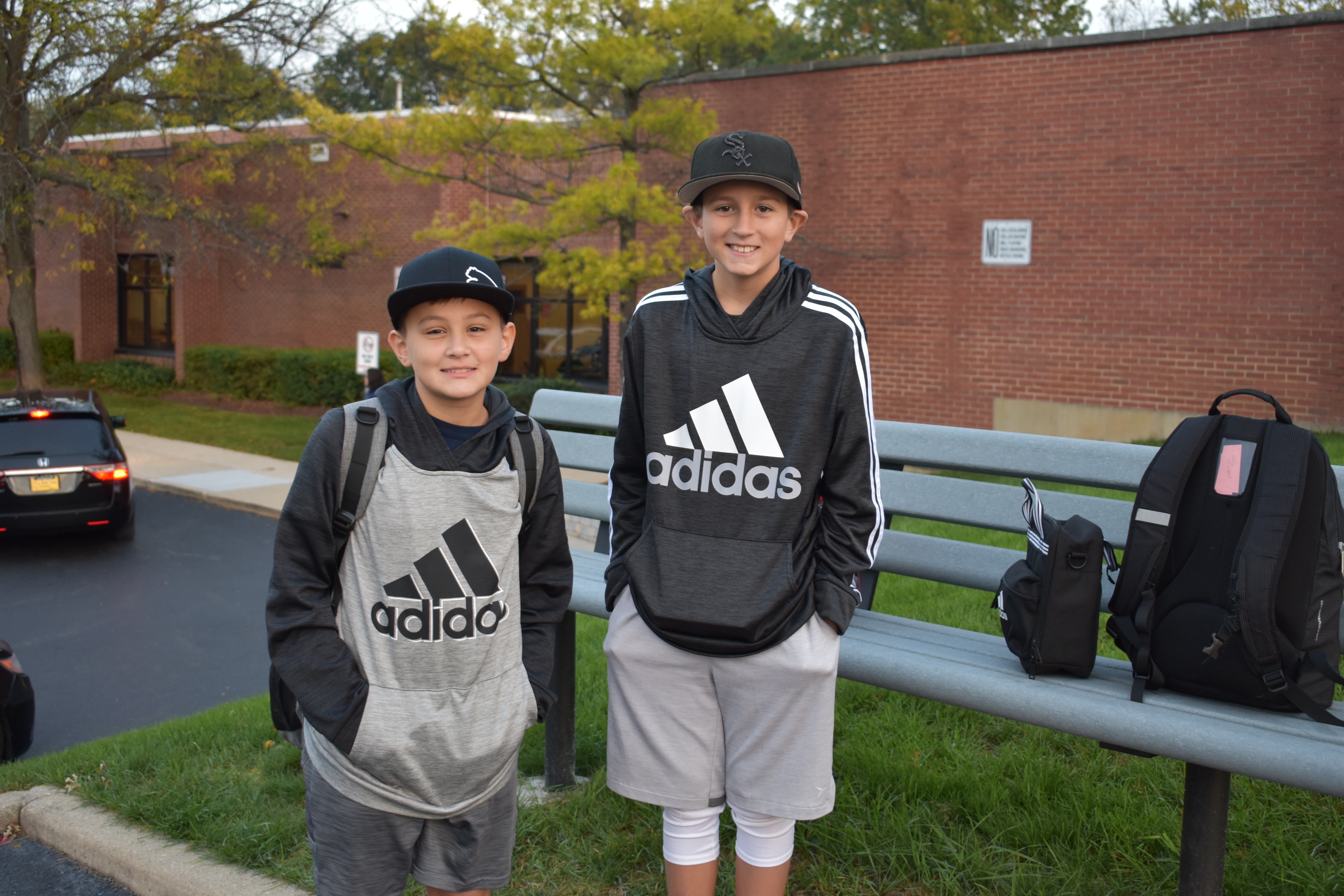 two students pose and smile on the blacktop in front of the school