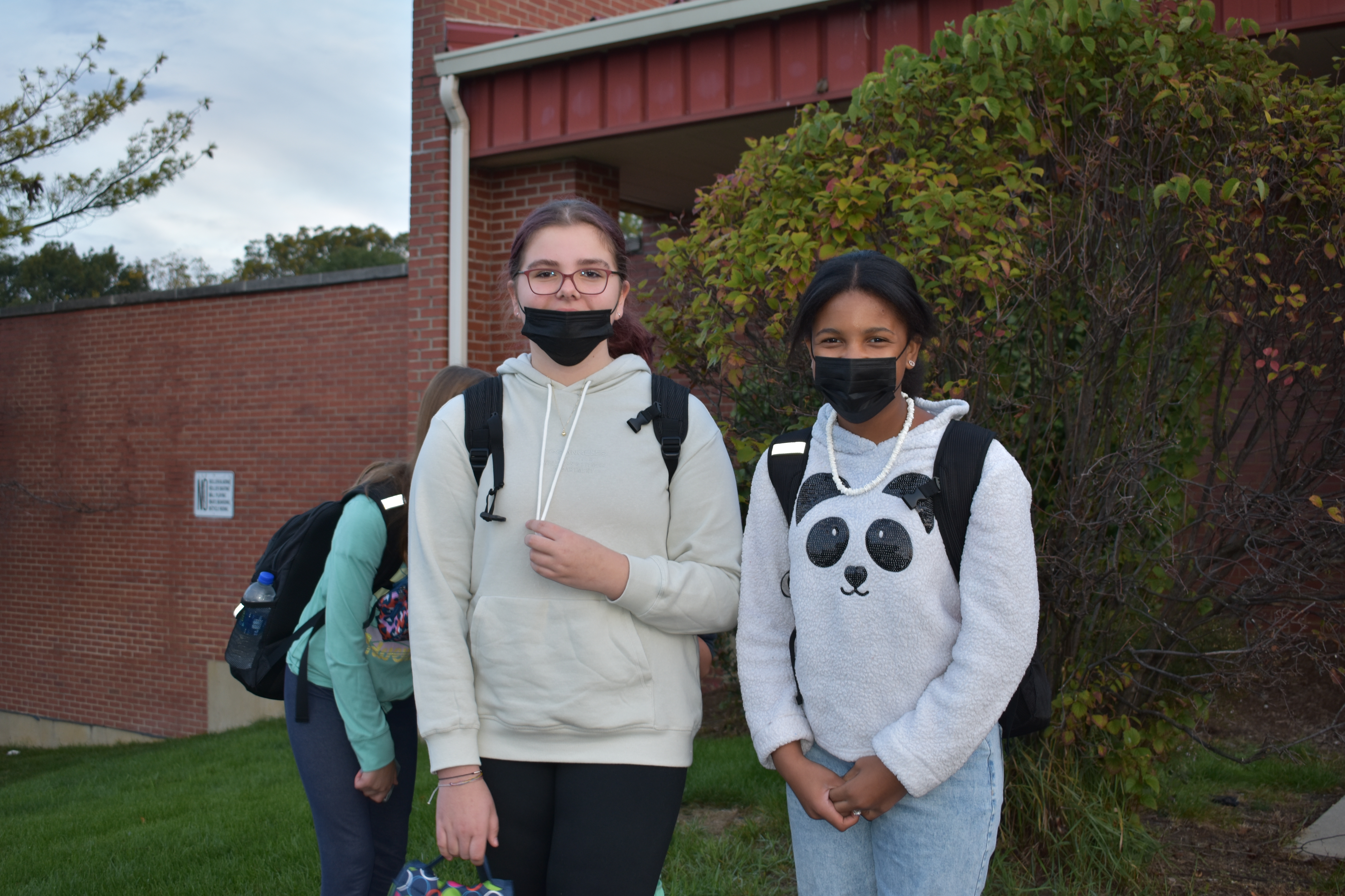 two more students pose and smile on the blacktop in front of the school