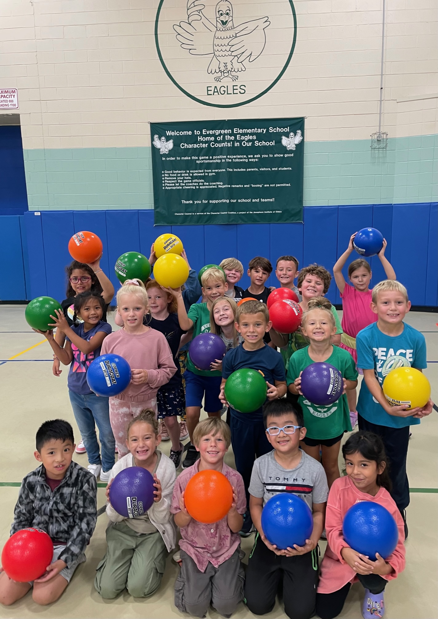 A large group of boys and girls holding colorful dodgeball balls