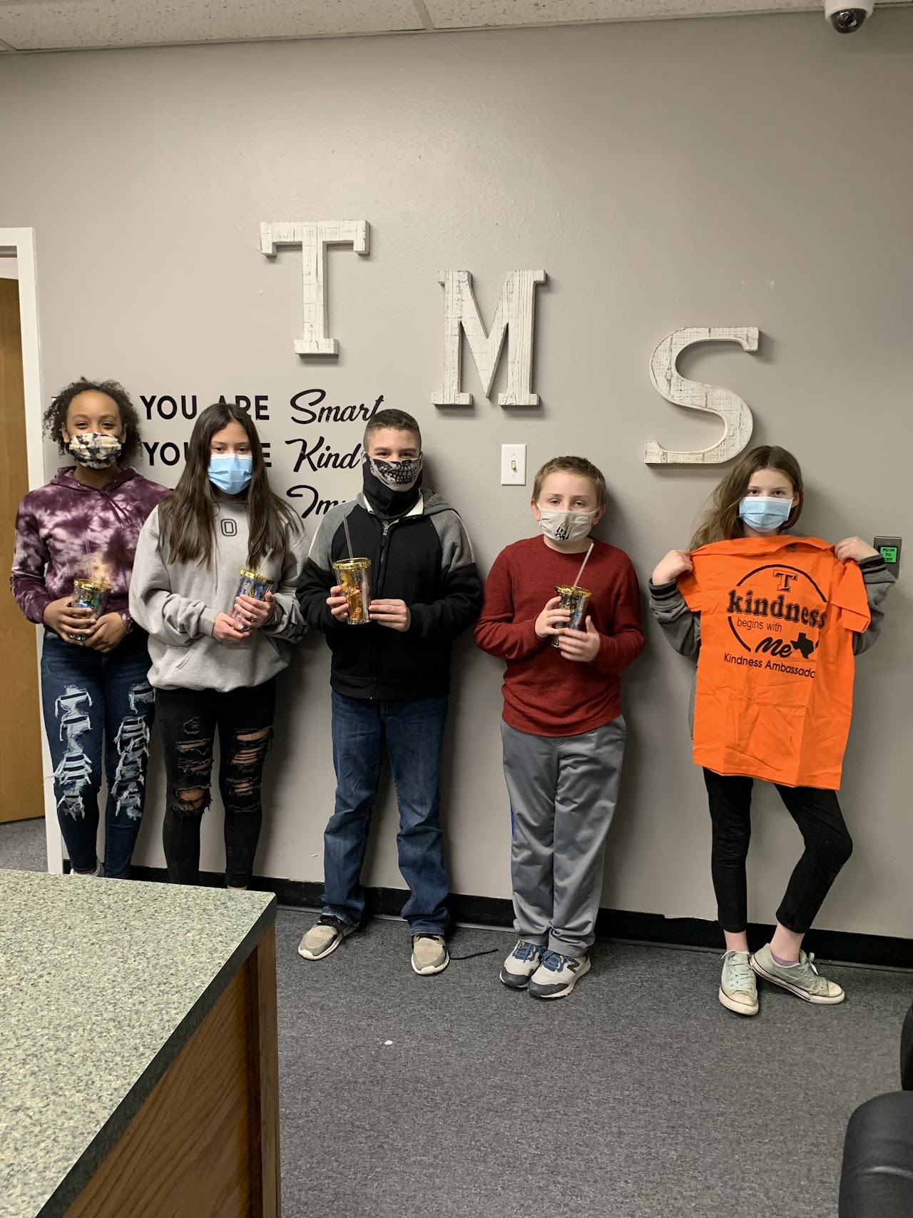 Five students with masks on holding cups and a t shirt