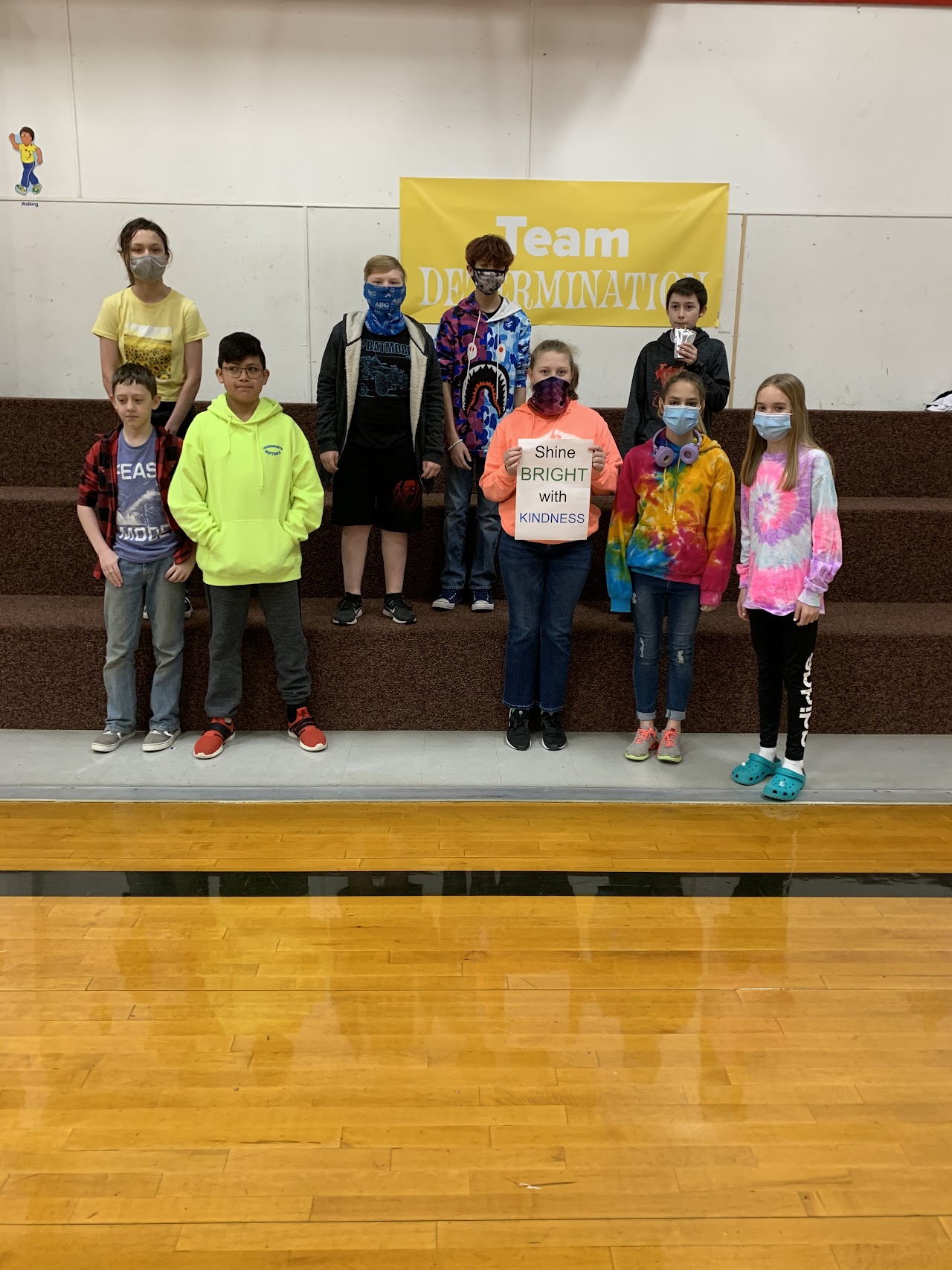 Students in a gym holding a sign that says shine bright with kindness