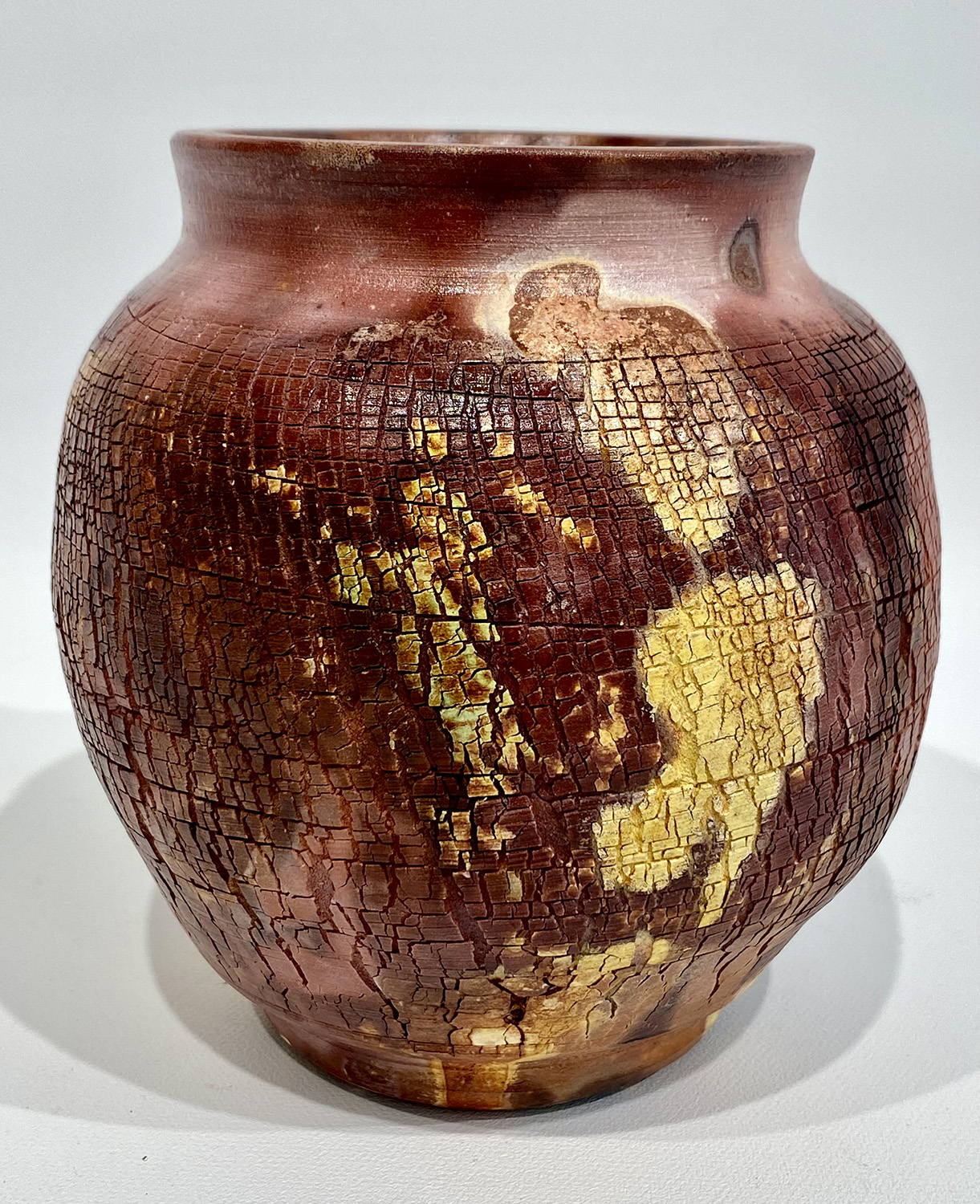 A ceramic pot with browns, blacks and yellows baked into its skin.