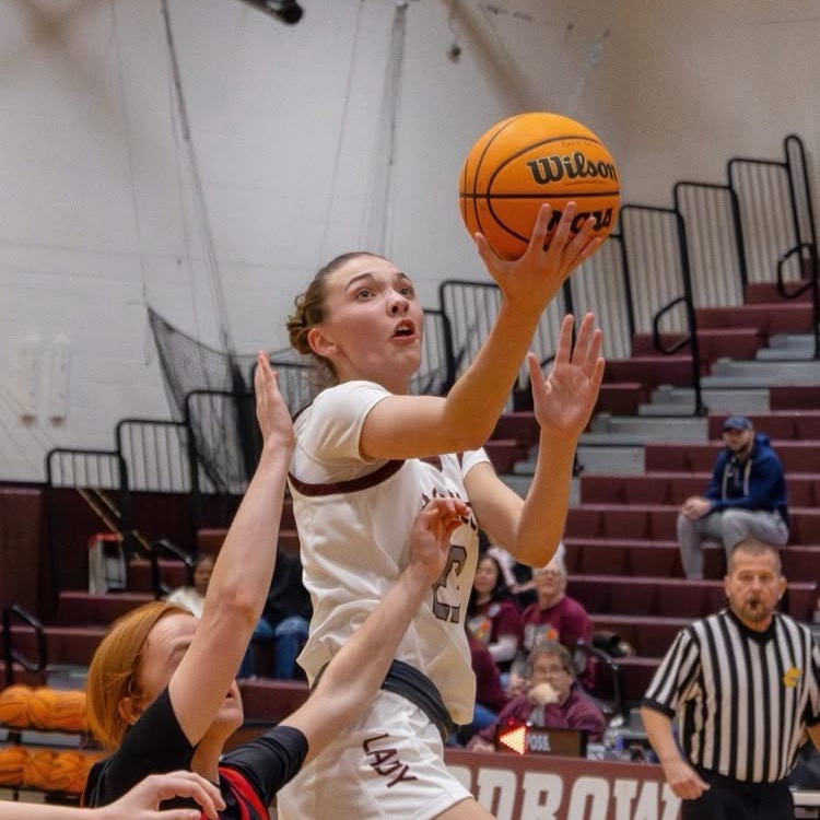 A female basketball player leaps to block a shot while another player attempts to steal the ball.