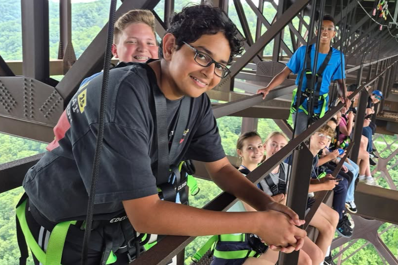 Group of young people in harness on a bridge, with one smiling, under a metal structure.