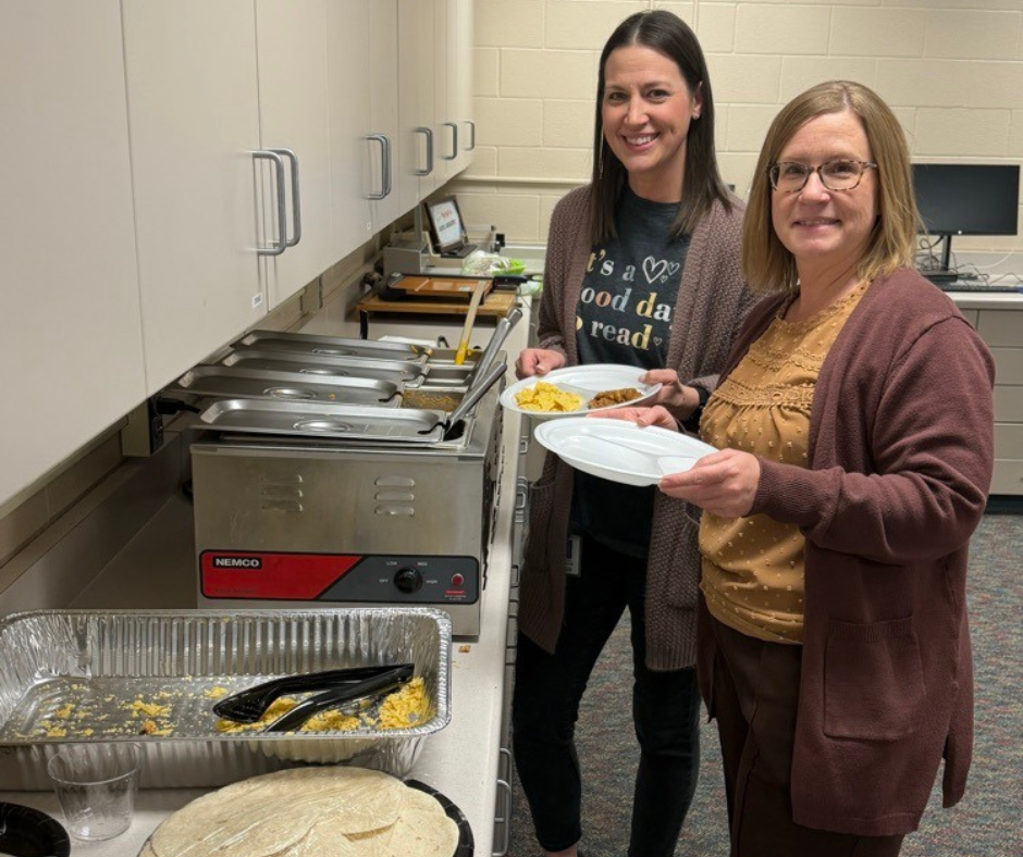 Two ladies smiling at a camera with a plate of food in hand