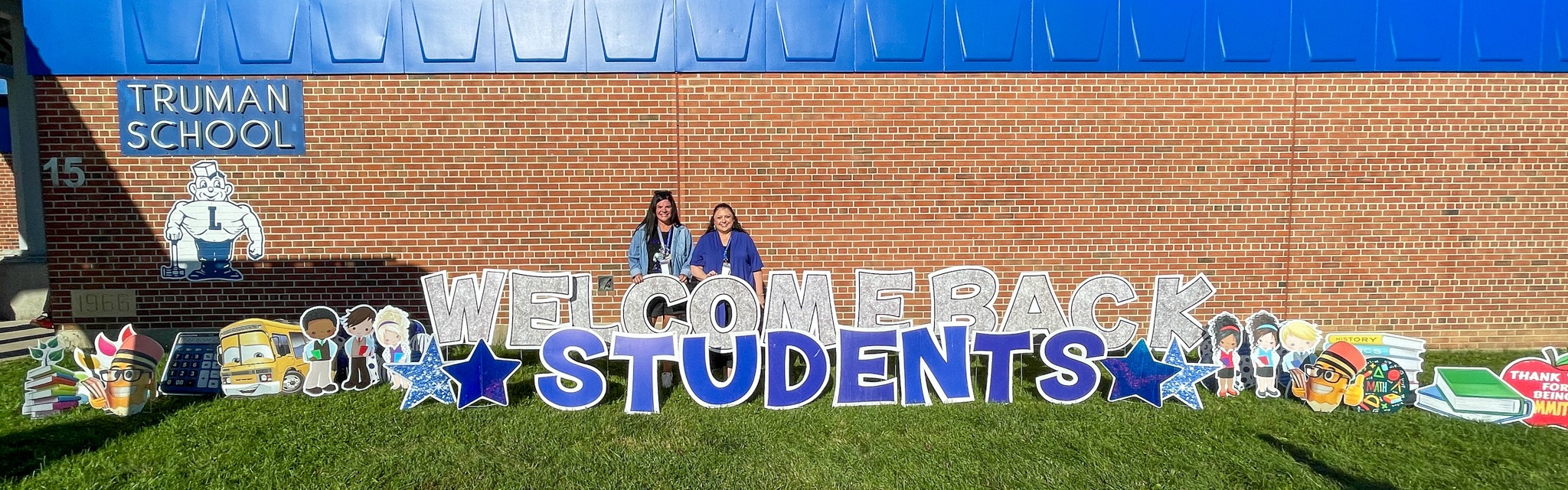 admins pose behind welcome back sign