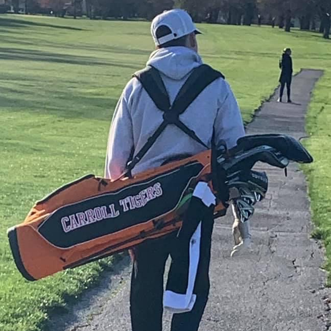 boy walking away with golf bag on