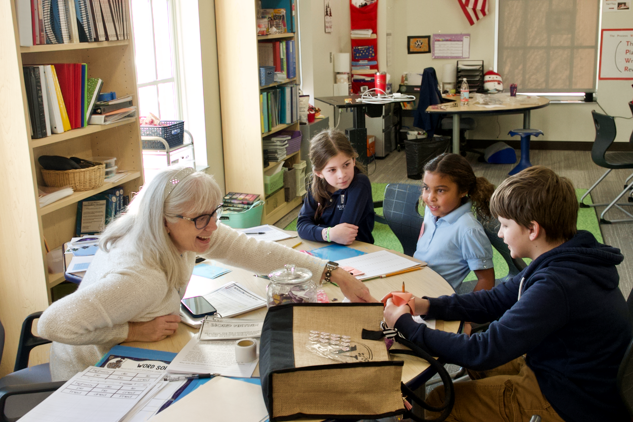 Teacher smiling at students sitting at a table while doing work.