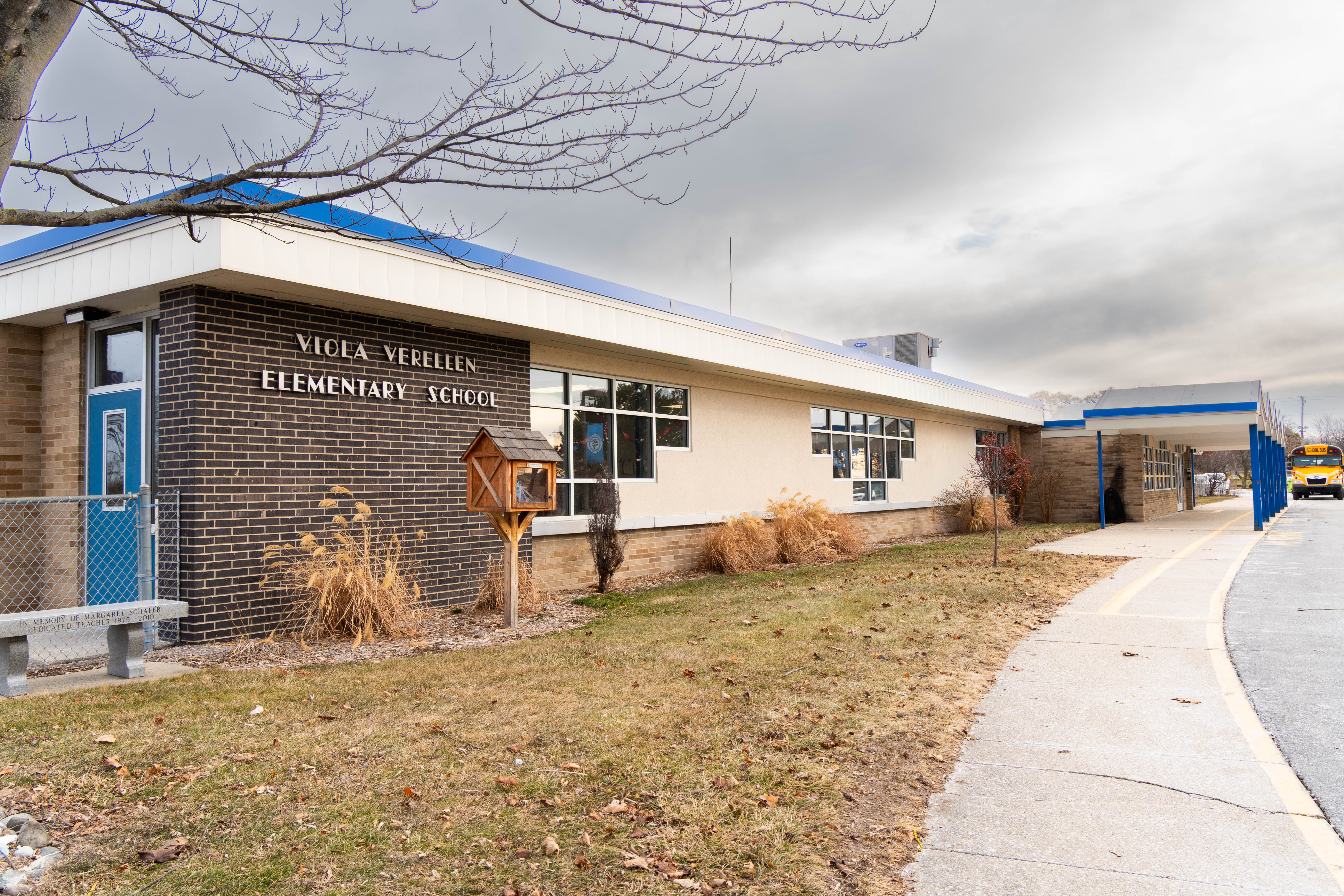 Exterior of Viola Verellen Elementary School with brick facade, blue trim, covered walkway, and a school bus visible near the entrance.