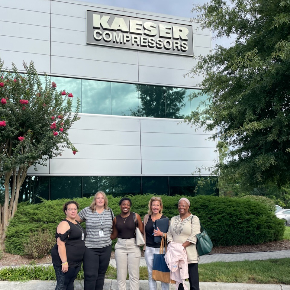 A group of employees posing and smiling outside of the Kaeser Compressors office building.