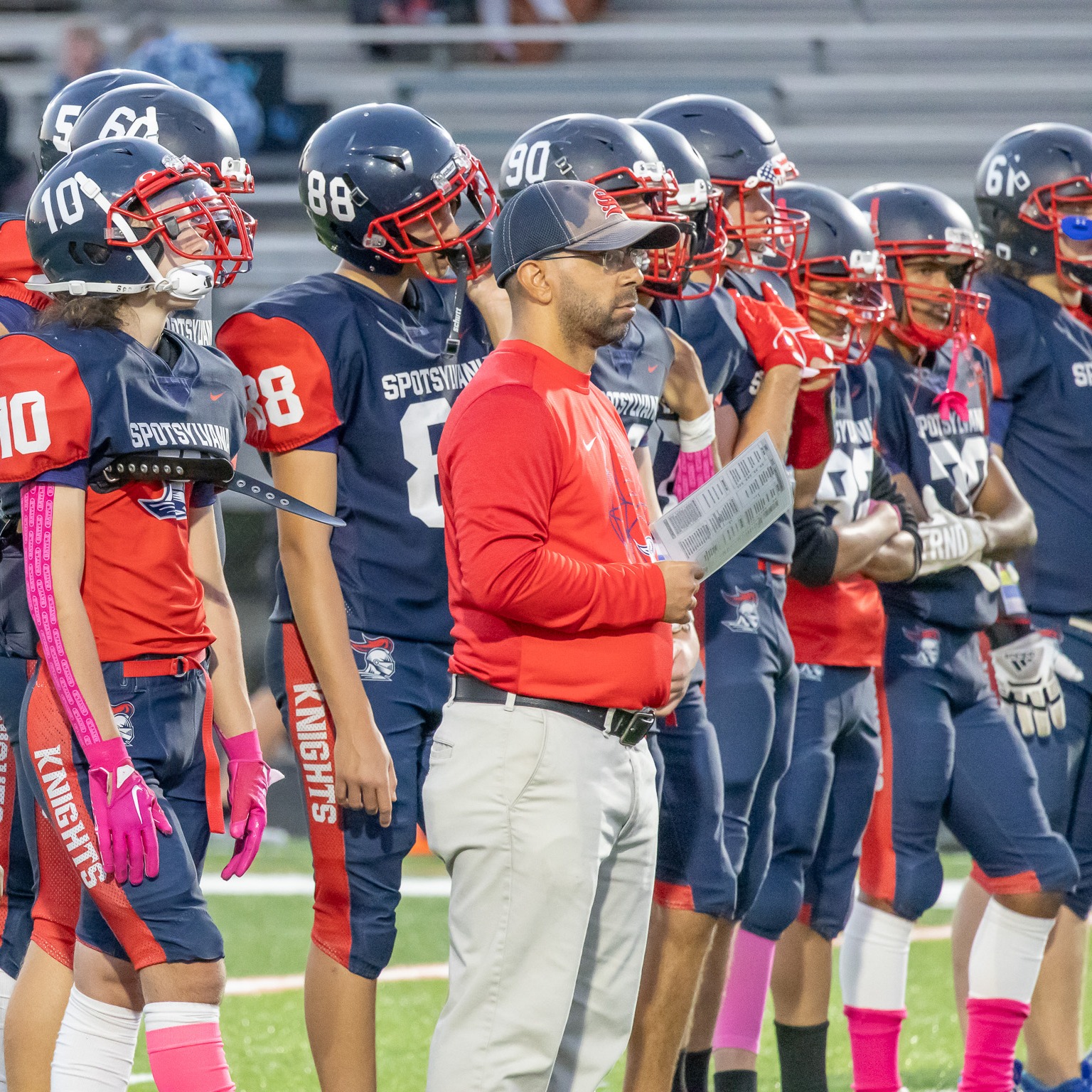 A group of football players wearing red and blue uniforms and helmets stand in a line on the field.