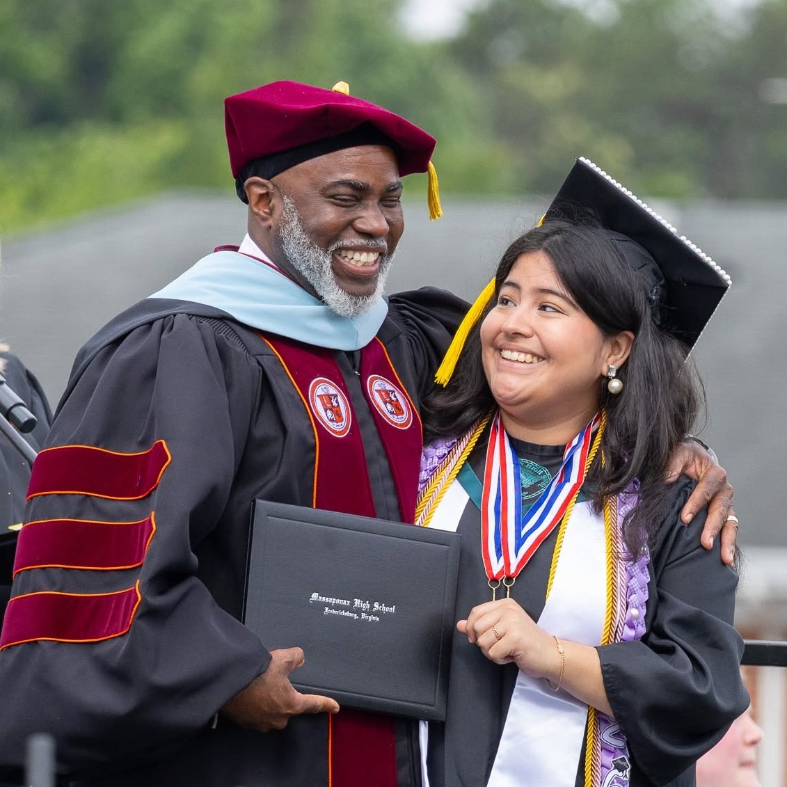 A person in a cap and gown receiving a diploma from a man in a graduation gown.