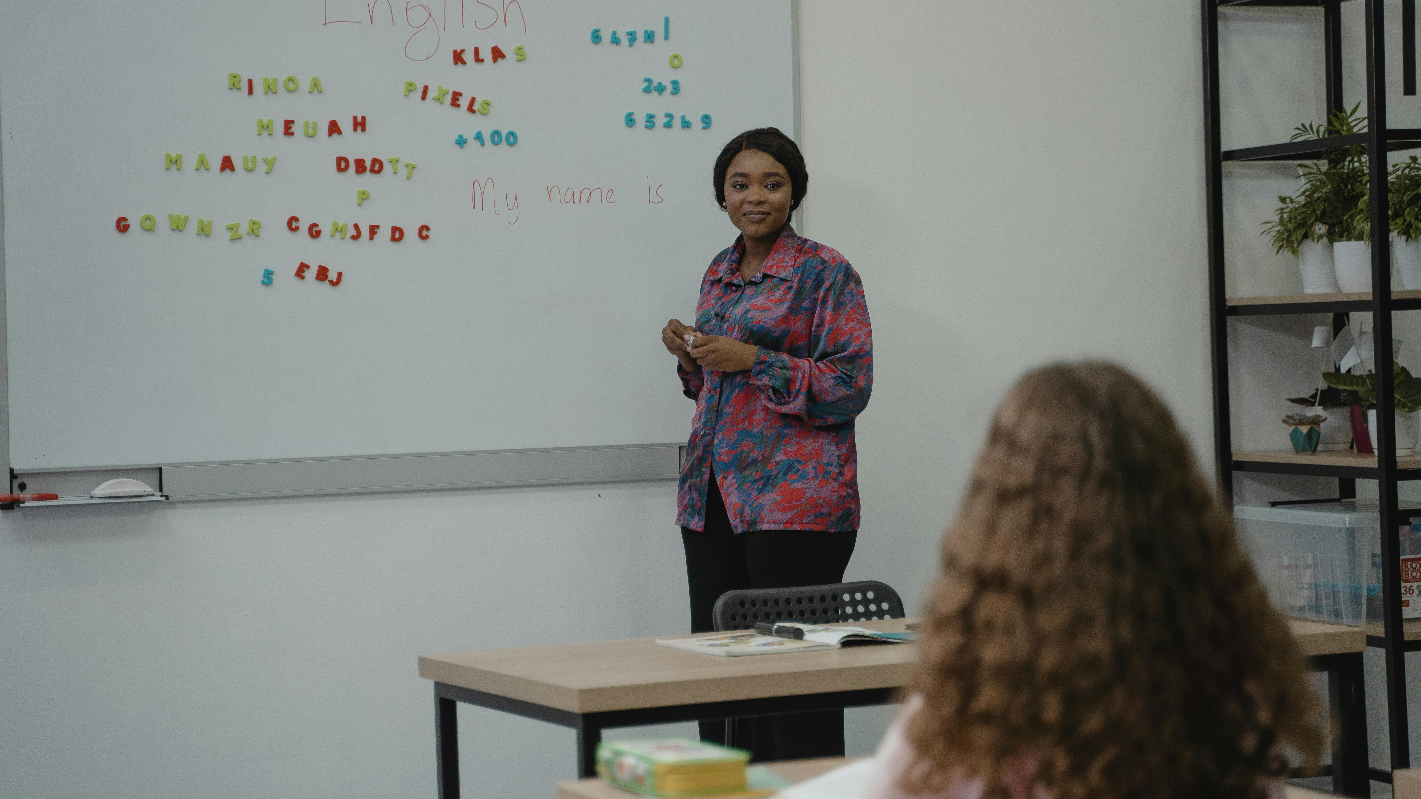 a teacher stands at a dry erase board and looks out at her student