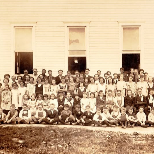 Black-and-white photograph of a large group of people in front of a building. Some are seated and others are standing.