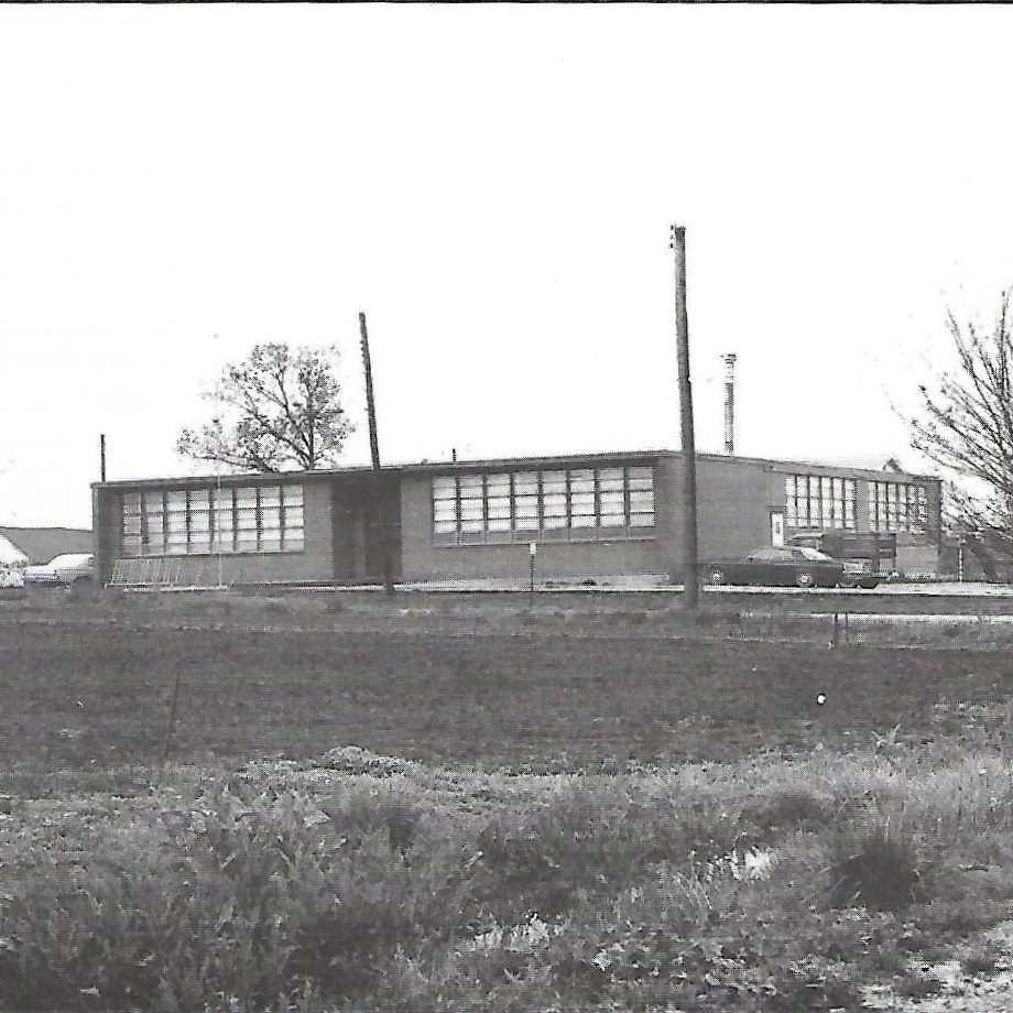 A monochromatic image shows a building with many windows, surrounded by a field of grass and trees.