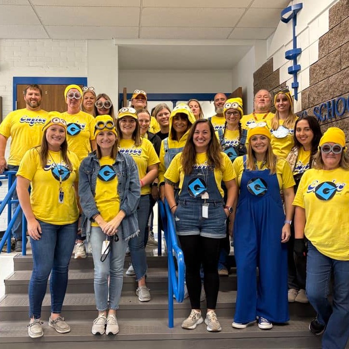 People in matching yellow costumes pose on a staircase with blue handrails, inside a building.