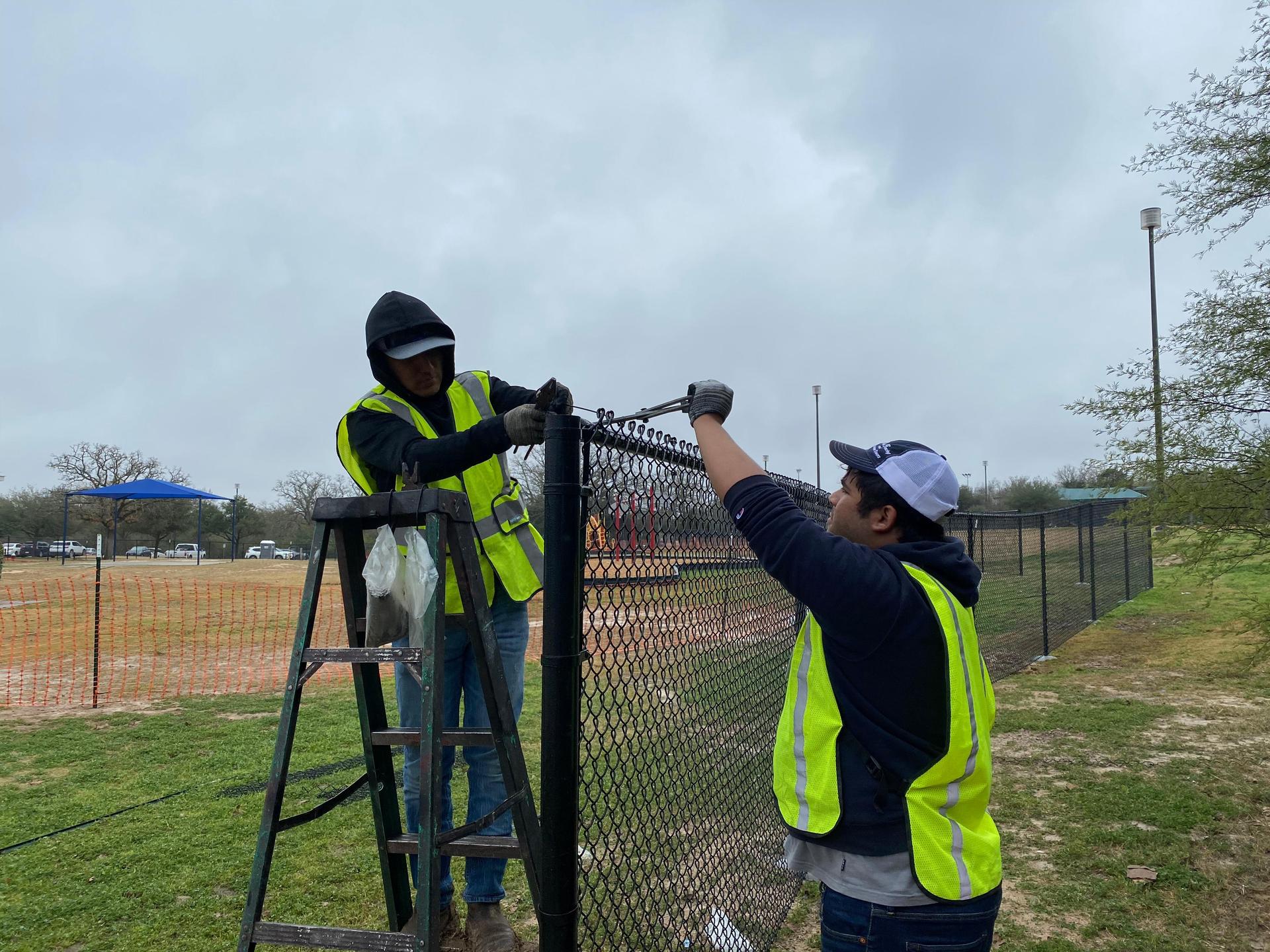 2 construction workers setting up a wire fence
