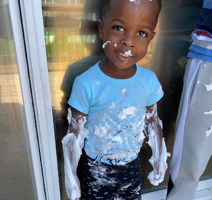 Child with shaving cream on arms, face and clothes.
